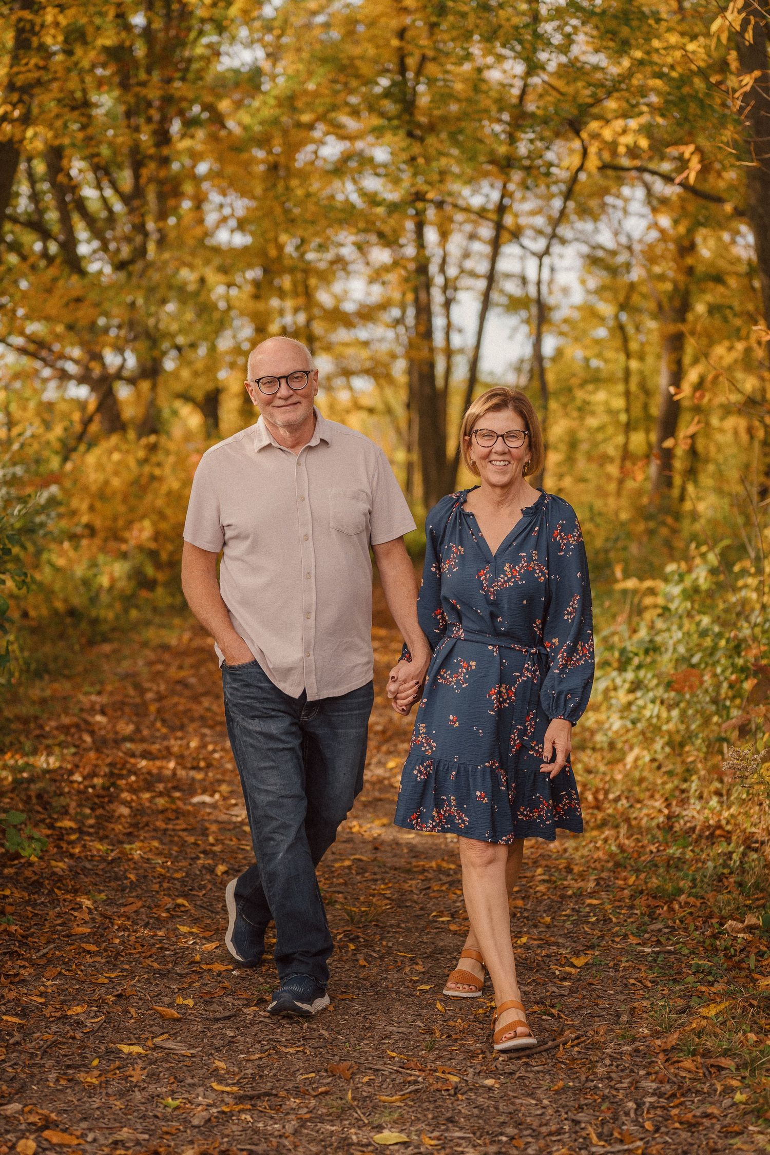 A couple walks together on a wooded trail surrounded by vibrant golden autumn foliage.
