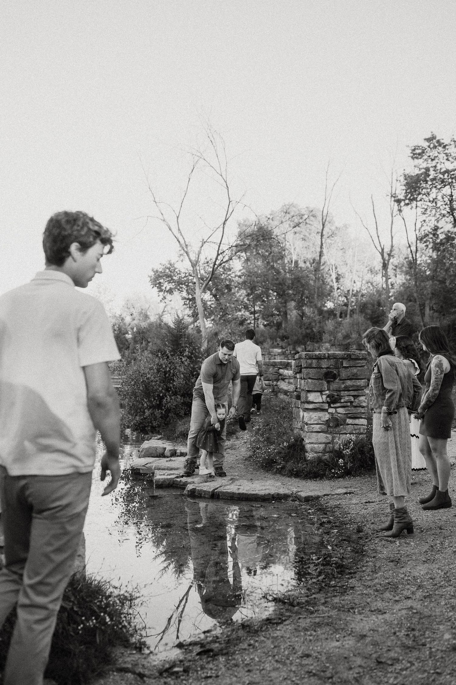 Vintage black and white photograph of people gathered near a stone wall outdoors.