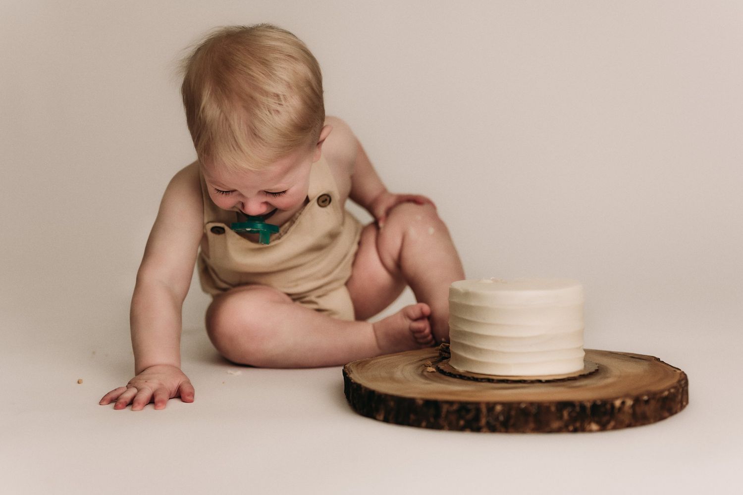 Small baby in beige outfit exploring a wooden coaster with a ceramic cup during a minimalist photo session.