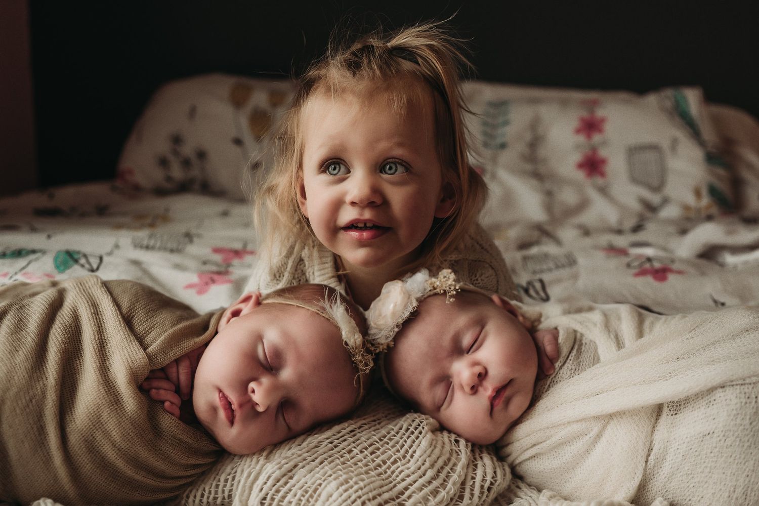Three children resting on patterned bedding with floral designs.