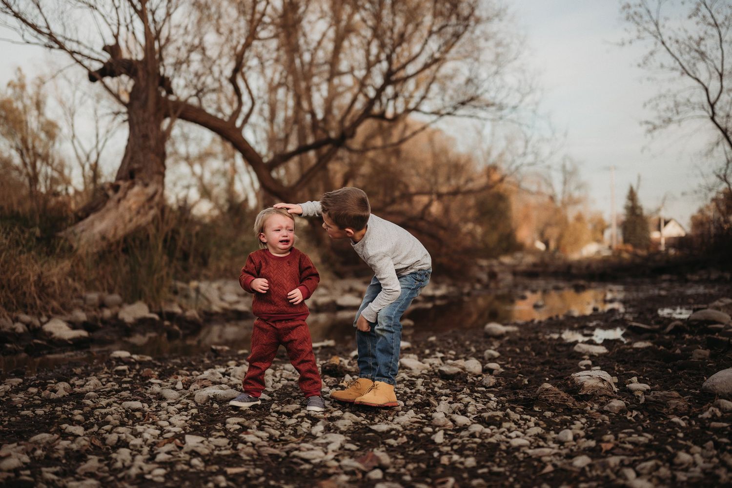 Children play together on rocky terrain during golden hour with bare trees in the background.