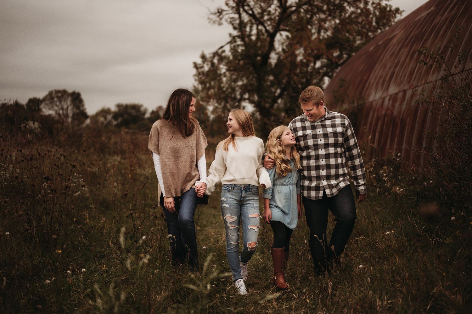 Family walks together through tall grass field during golden hour.