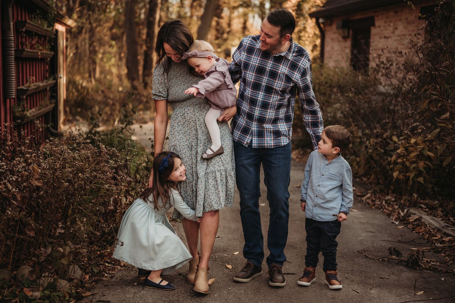 Family walking together on a rustic path surrounded by autumn trees and red fence.