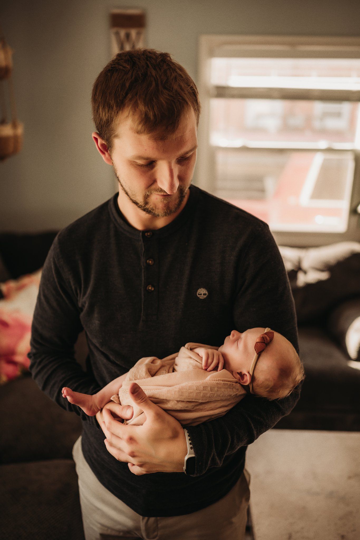 A tender moment as a parent in a black sweater cradles their sleeping newborn baby in a cozy living room setting.