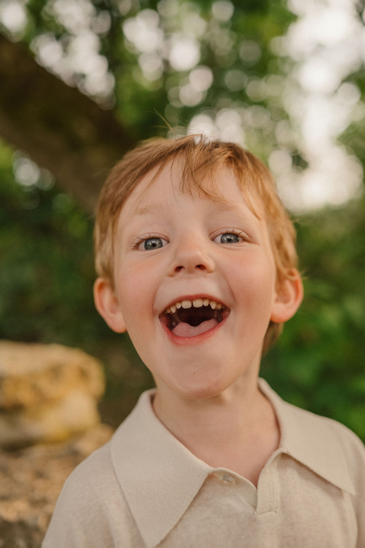 A candid portrait capturing pure joy and laughter against a soft bokeh background of green foliage.