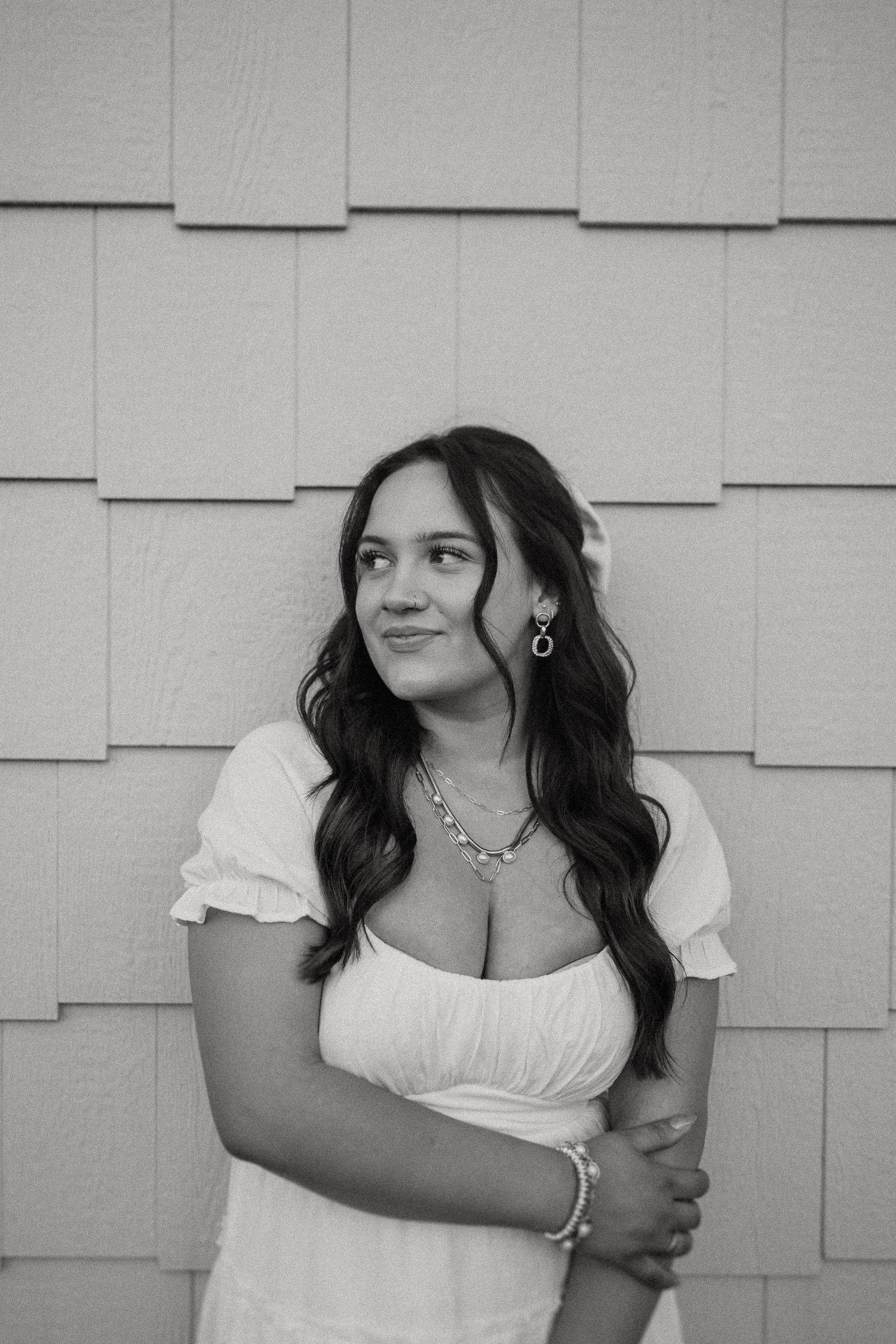 Black and white portrait against textured wall wearing white summer dress with jewelry accents.