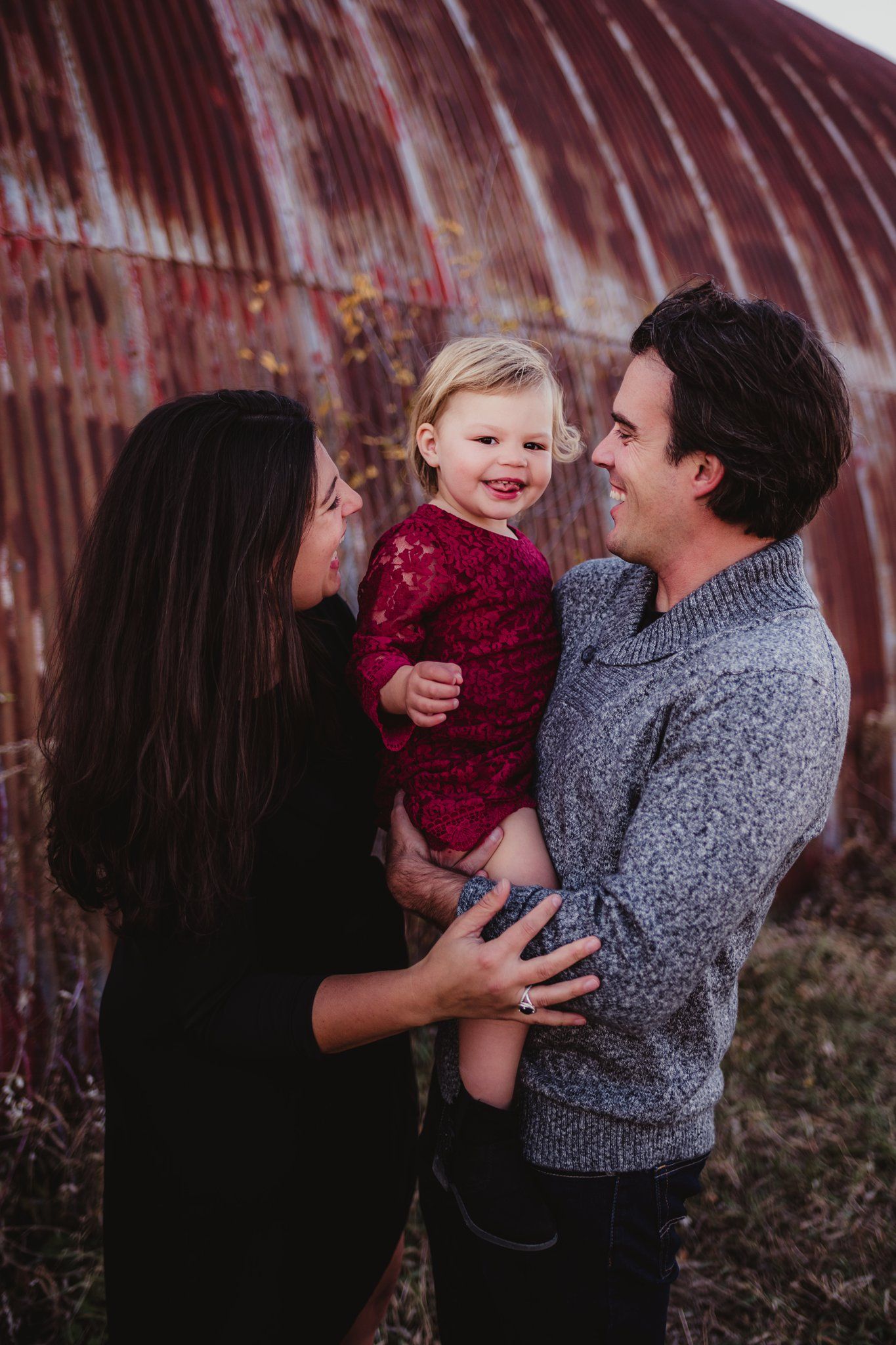 Family sharing loving moment by rustic barn wall during portrait session.