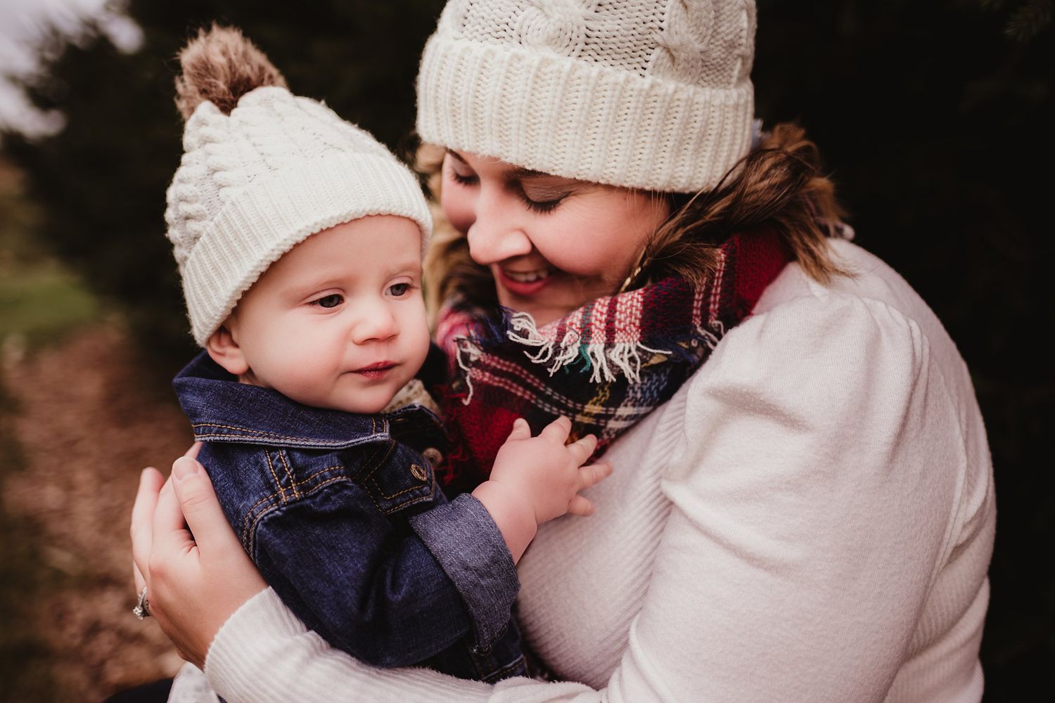 Close-up winter portrait of parent and baby wearing matching white knit hats.