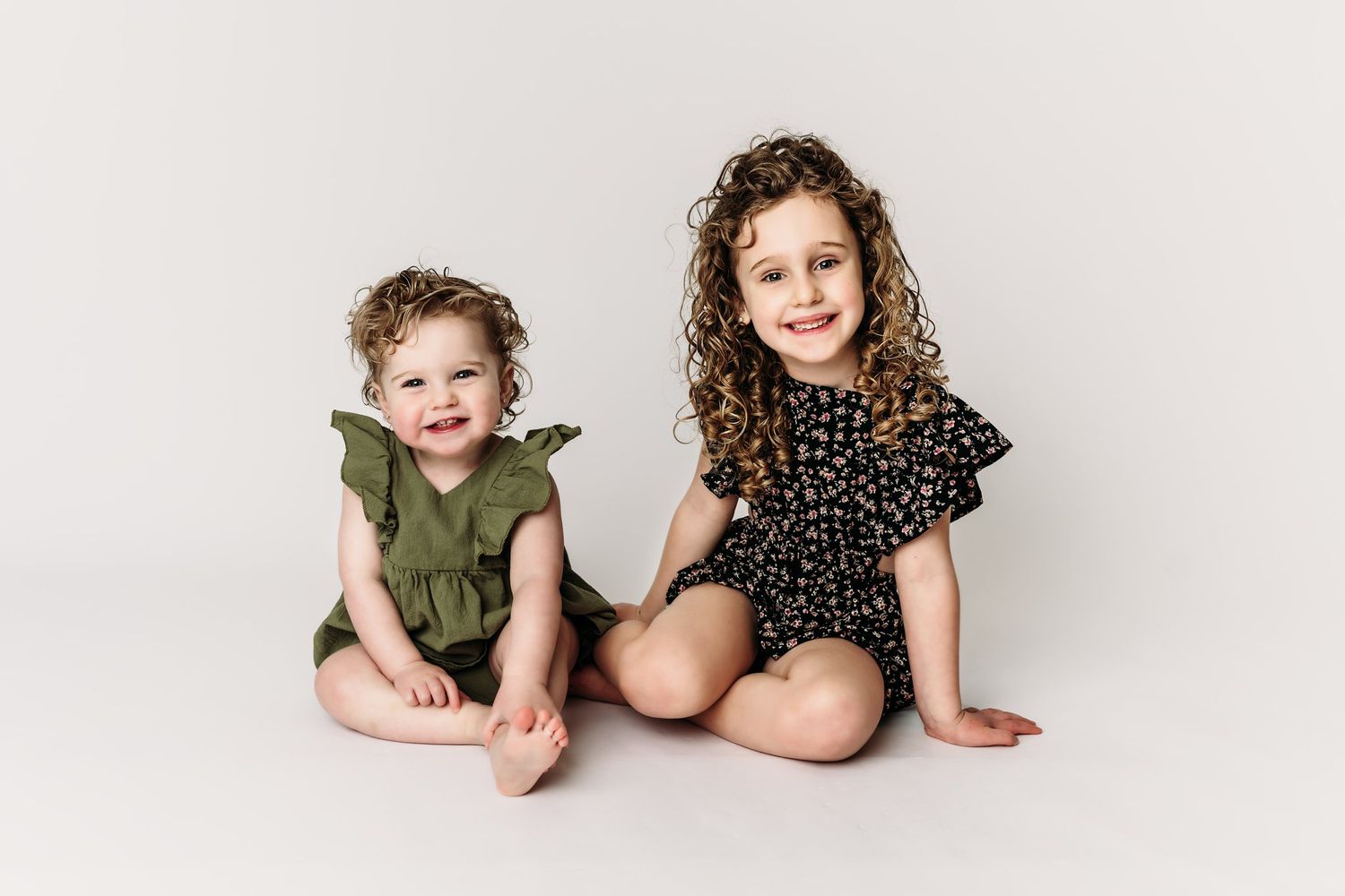 Two children sit casually together on white background in coordinating outfits.