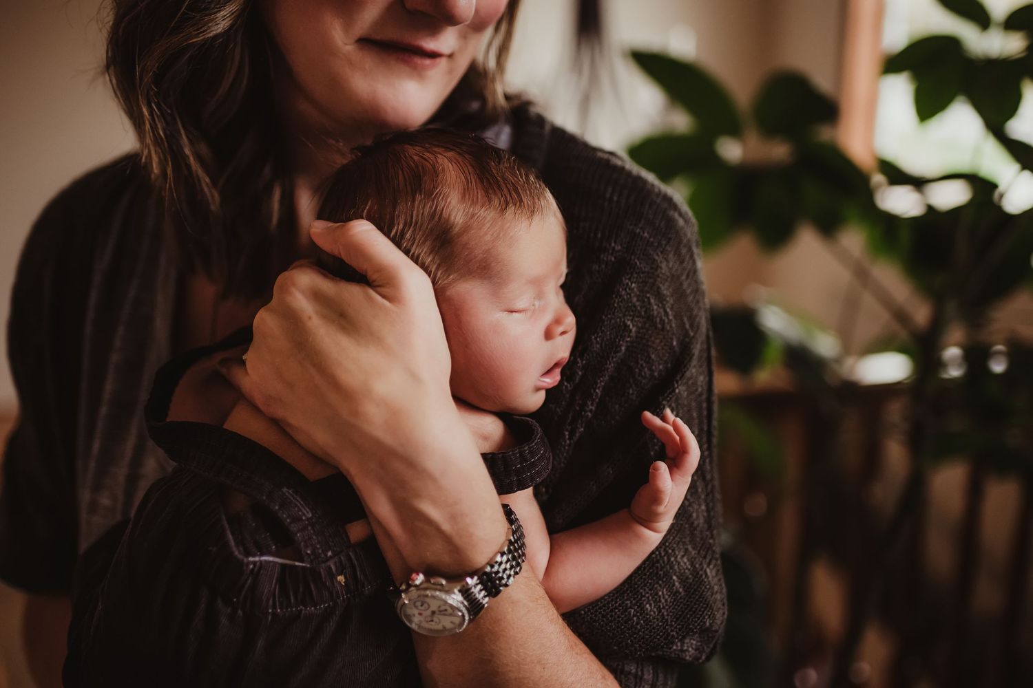 An intimate moment shows a baby being held close in a dimly lit indoor setting.