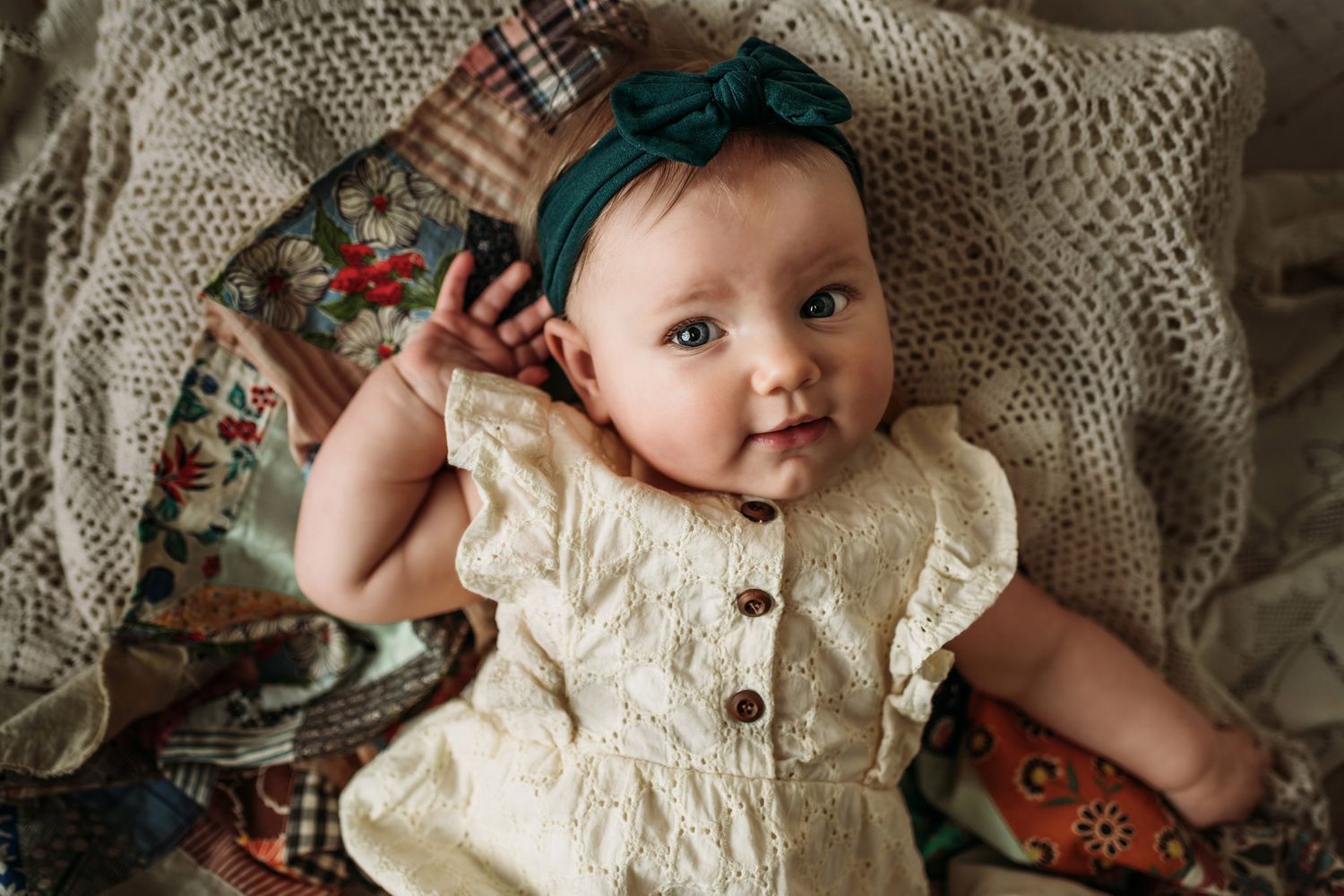 Overhead view of infant in cream dress lying on knit blanket with floral accents.