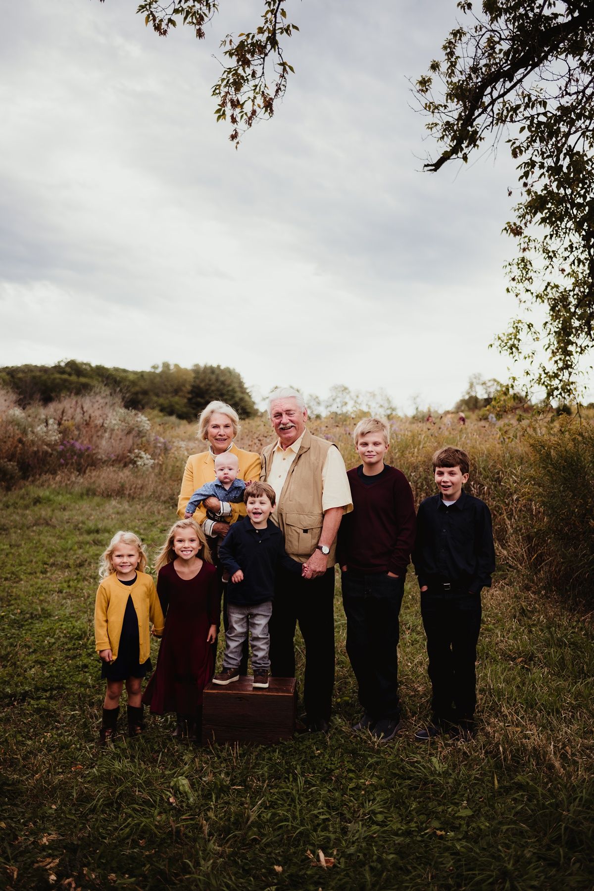 Extended family gathering outdoors on a hillside with autumn foliage in the background.