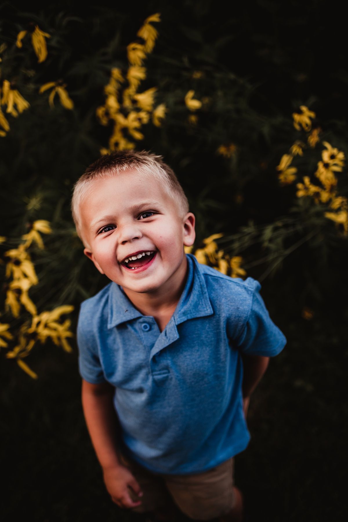 Candid portrait of child in blue polo shirt laughing against dark background with yellow leaves.