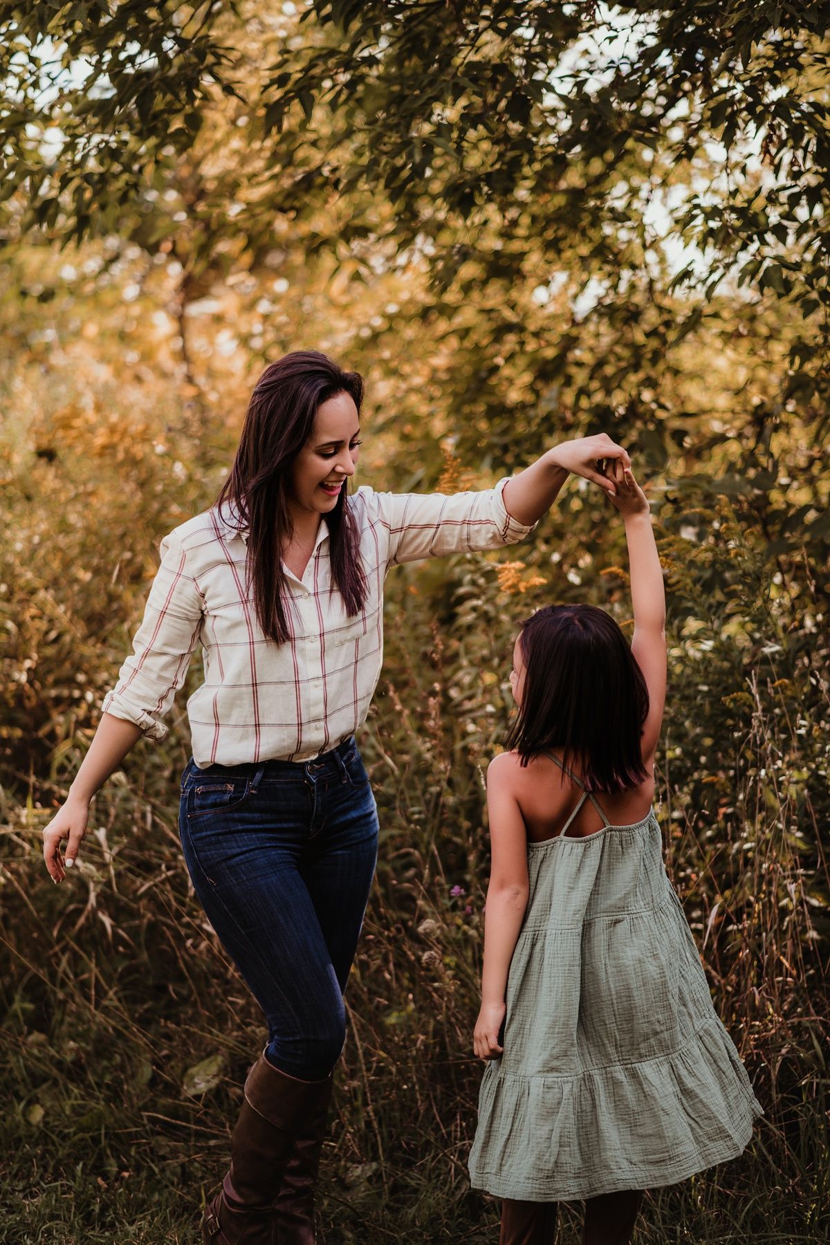 Parent and child dancing together in nature during golden hour among autumn trees.