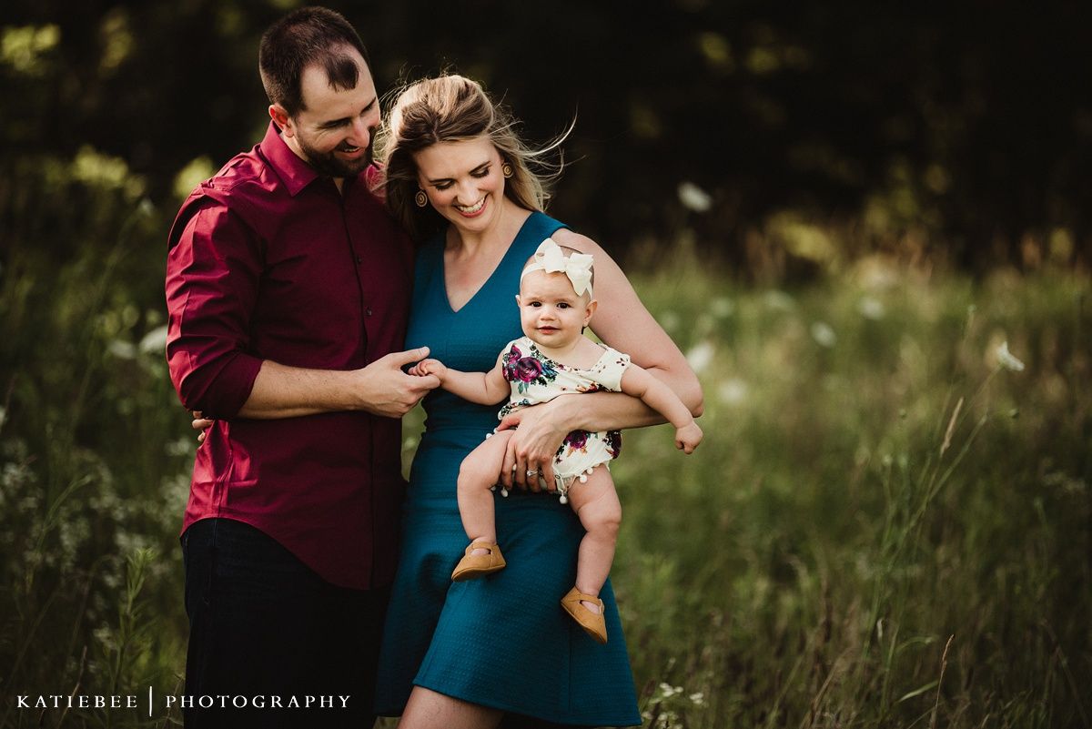 Family portrait in a meadow with burgundy and teal clothing.