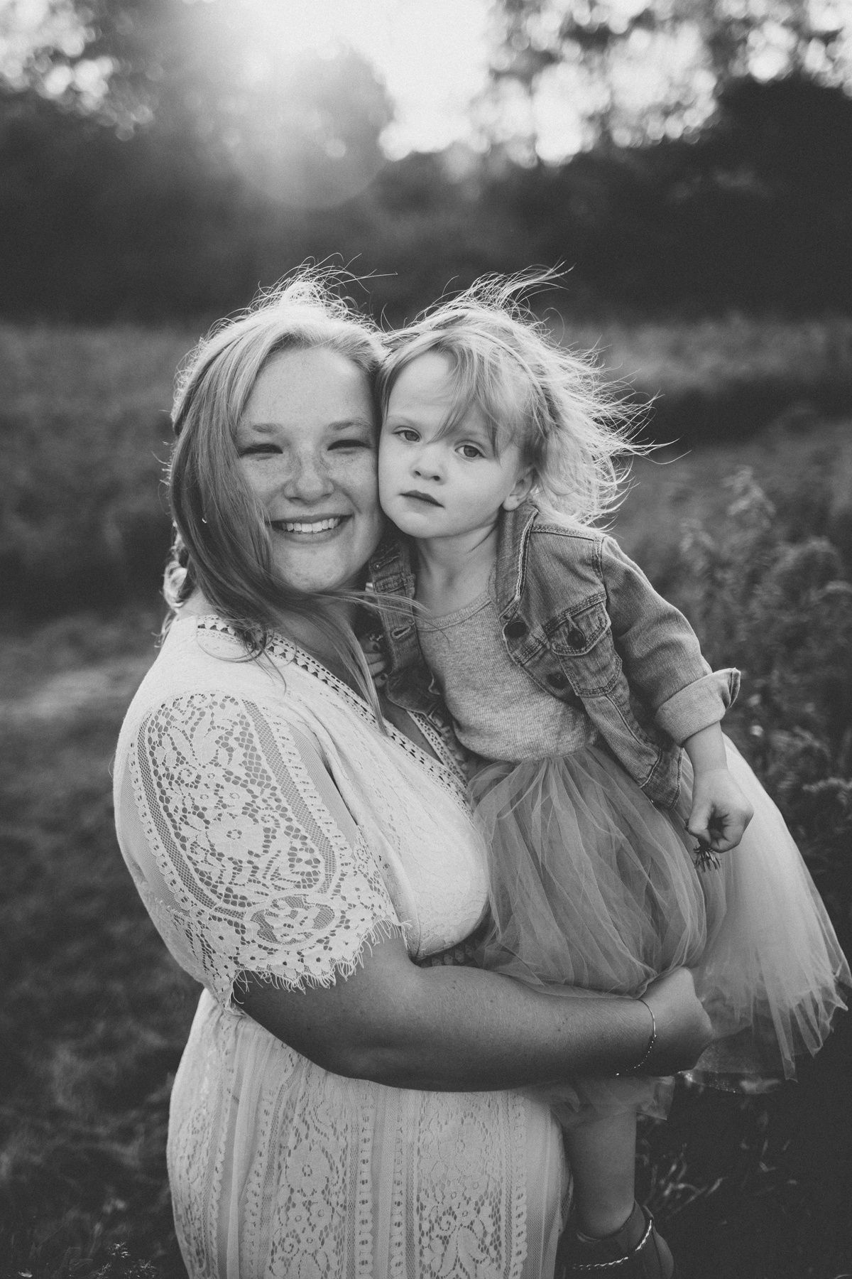 Black and white portrait of a tender moment between parent and child in a sunlit meadow.
