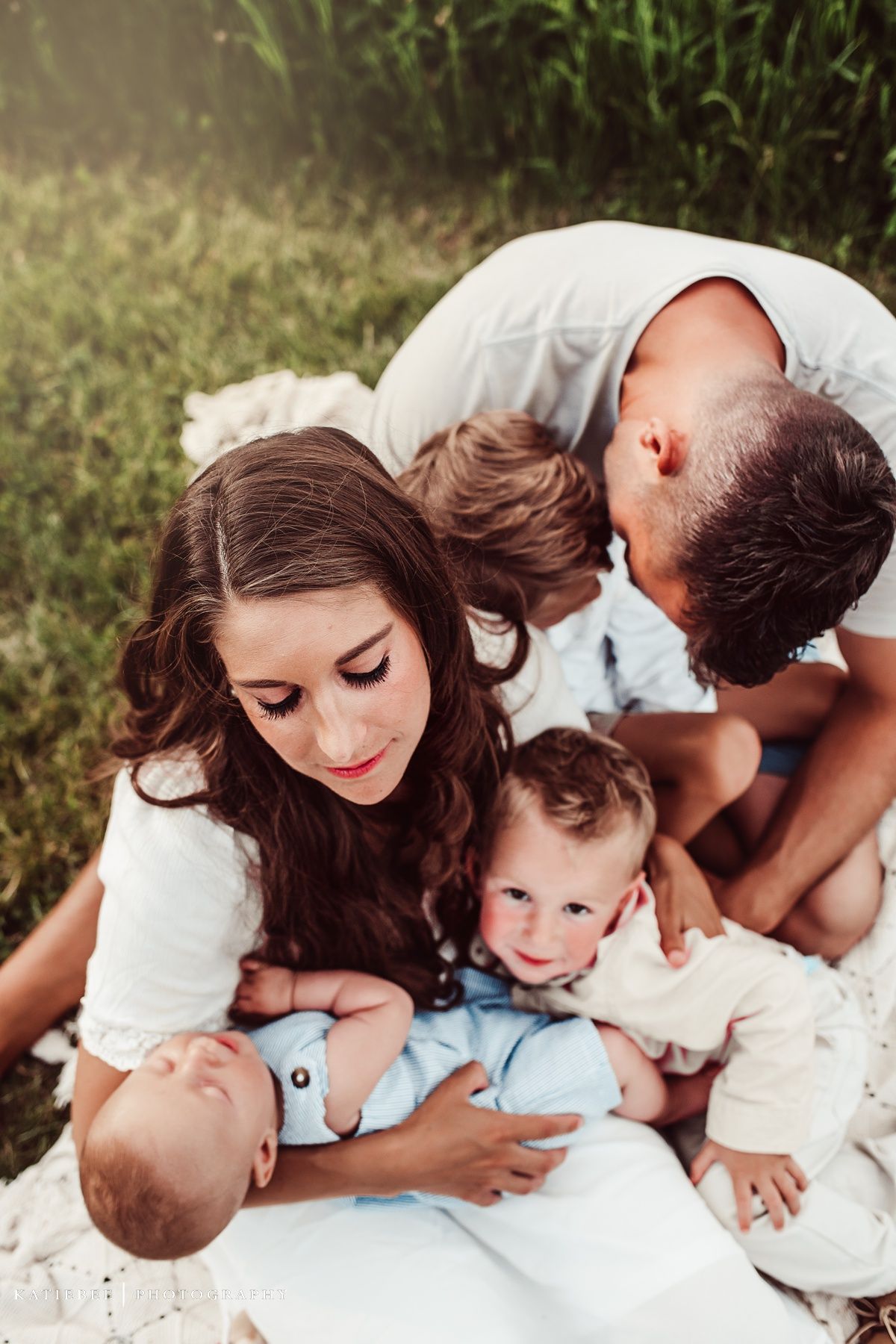 Close-up family moment captured on white blanket in natural outdoor setting with warm sunlight.
