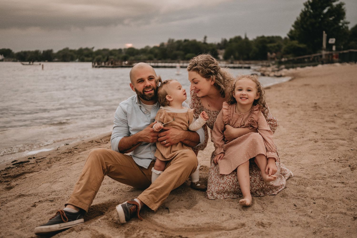 A candid family portrait on the beach with people sitting together on the sand at dusk.