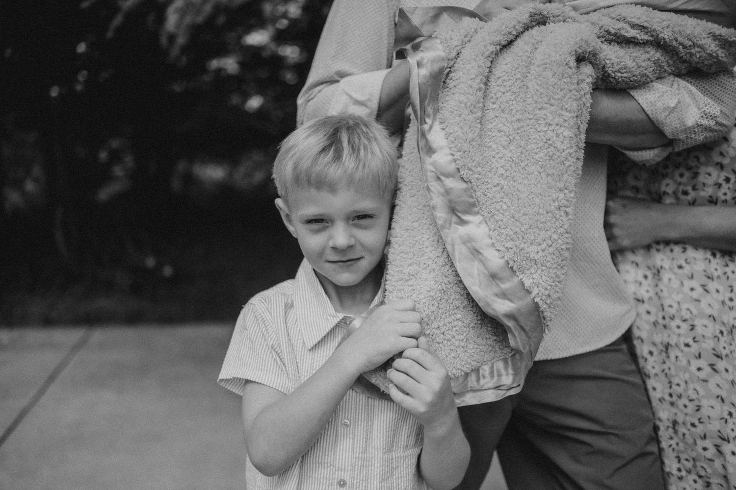 Black and white image of a young child holding onto a wrapped bundle outdoors.