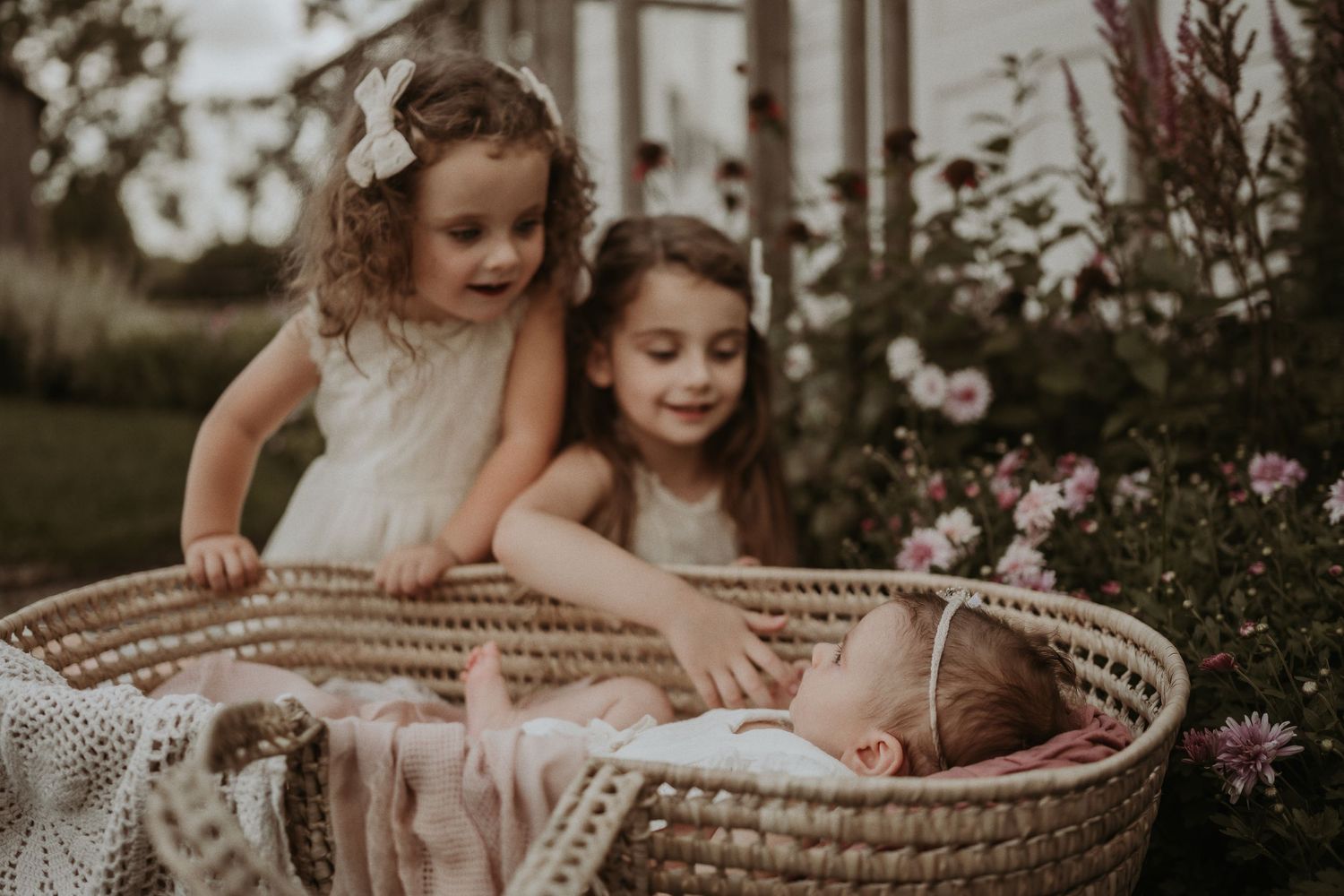 Vintage-style photo of children looking into woven basket among pink flowers.