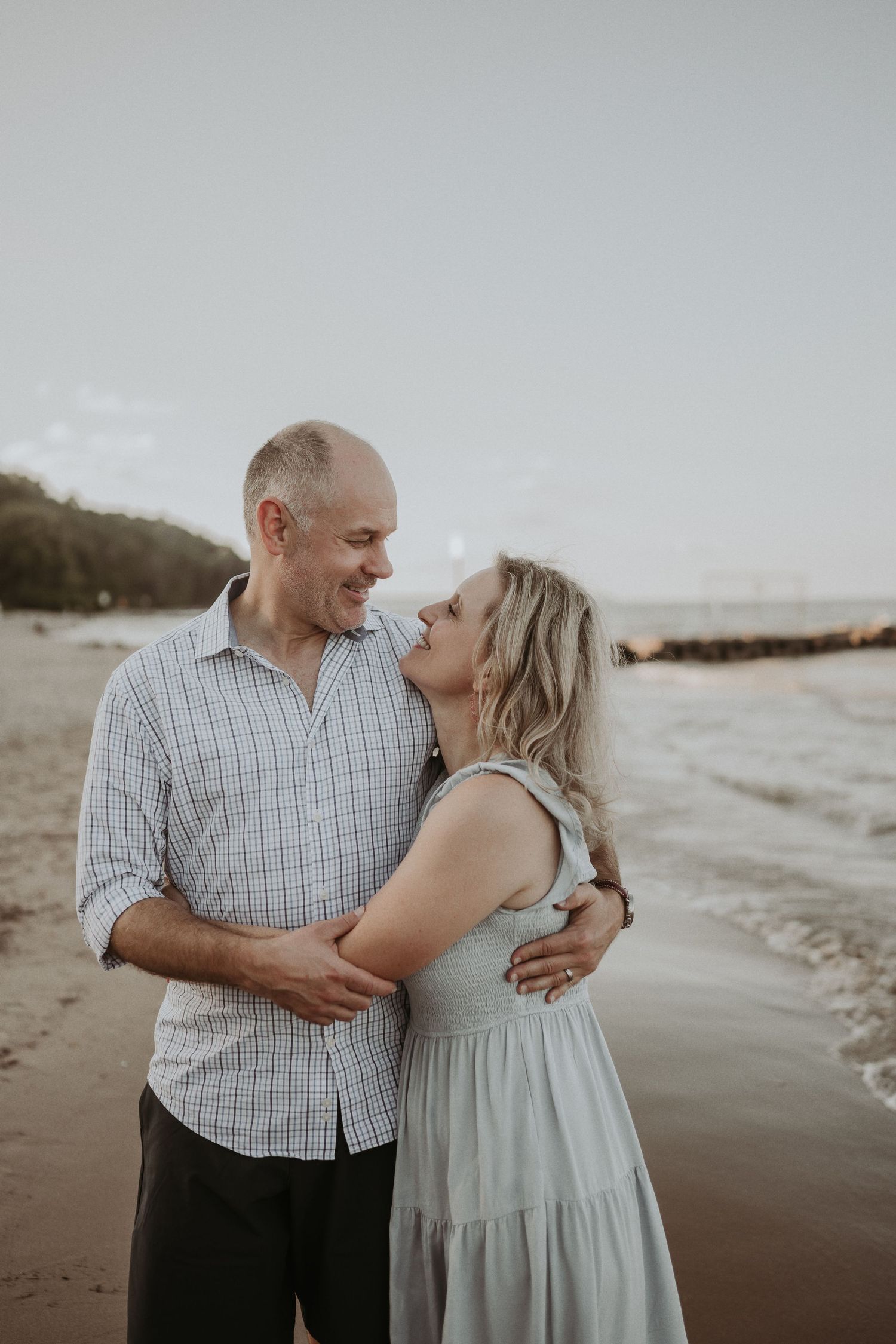 Romantic couple embracing and laughing together on a cloudy beach at sunset.