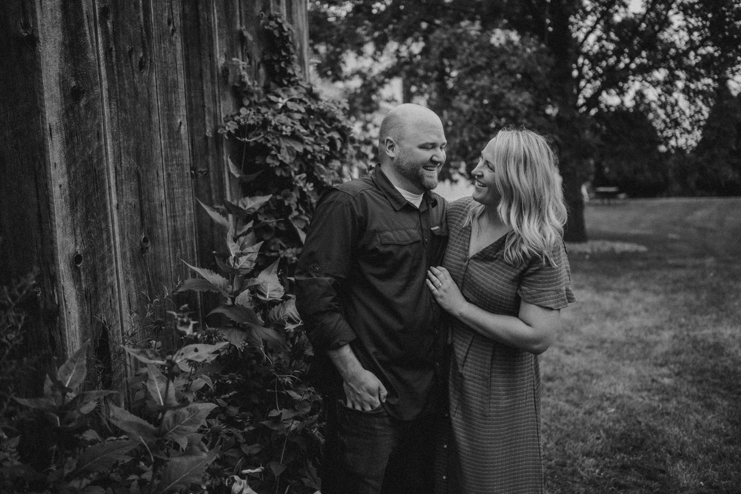 Black and white portrait of a couple sharing an intimate moment against a rustic wooden wall outdoors.