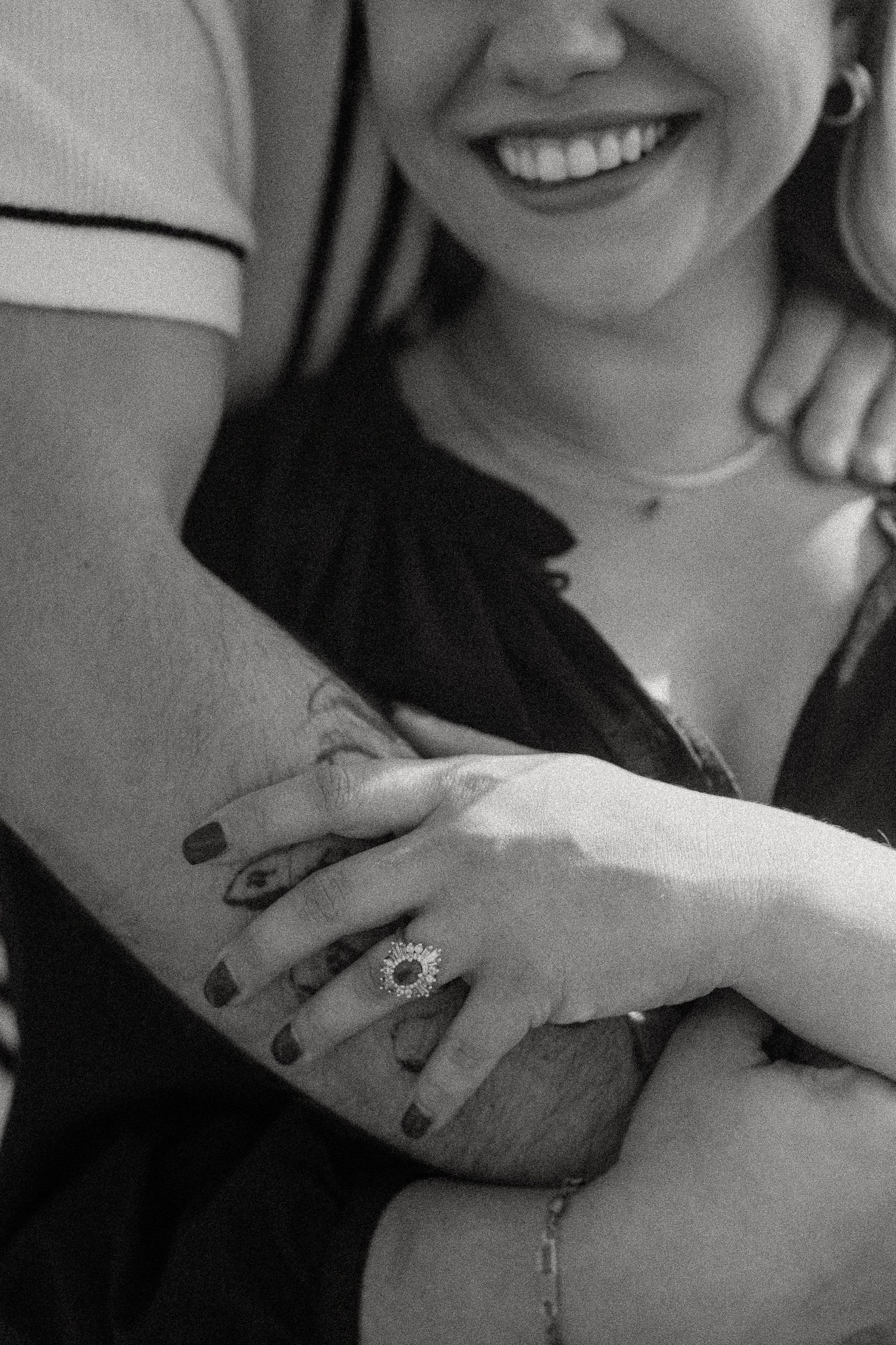 A close-up black and white photo showing hands with engagement ring and tattoos.