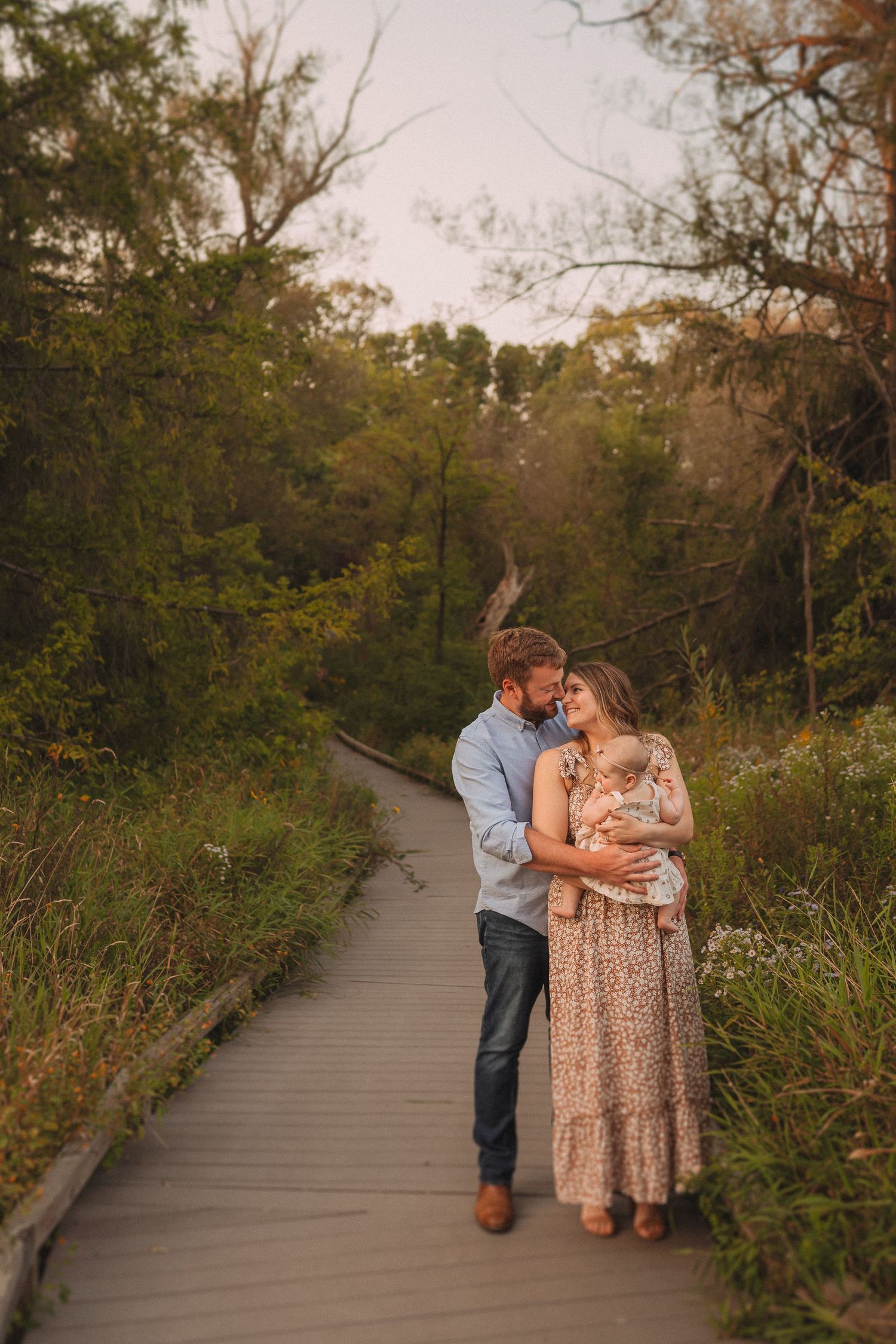 A tender embrace between two people on a wooden boardwalk surrounded by autumn foliage at sunset.