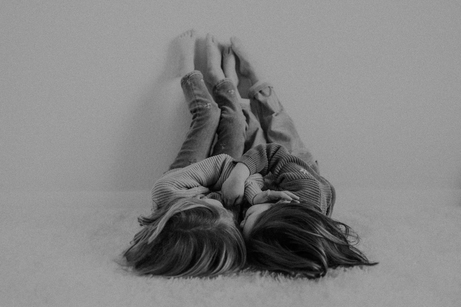 Two people in matching sweaters lie head to head on a white background in black and white.