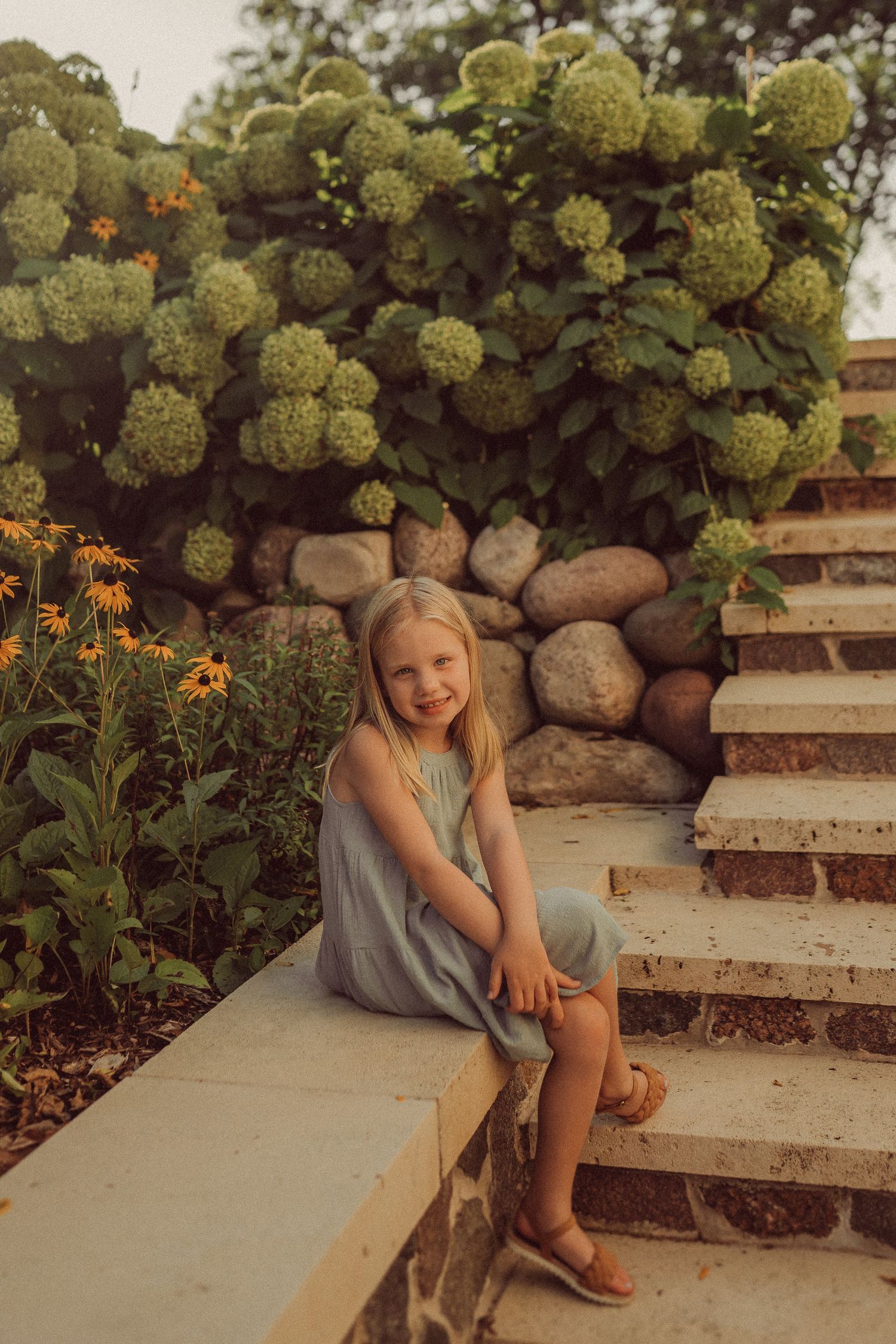 Garden portrait at sunset with stone steps, flowering bushes and orange blooms.