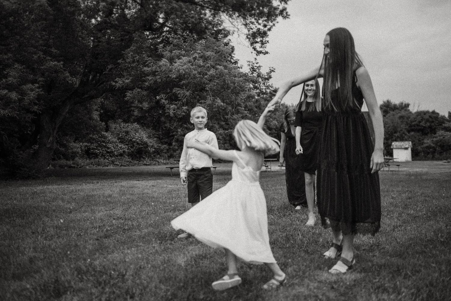 Black and white photo of people dancing and playing in a grassy field on a cloudy day.