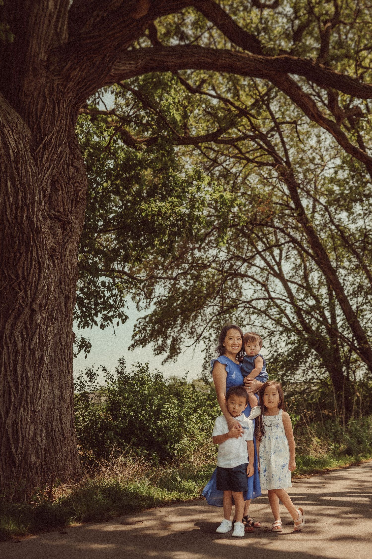 A family stands together on a tree-lined path during sunset, framed by an overhanging branch.