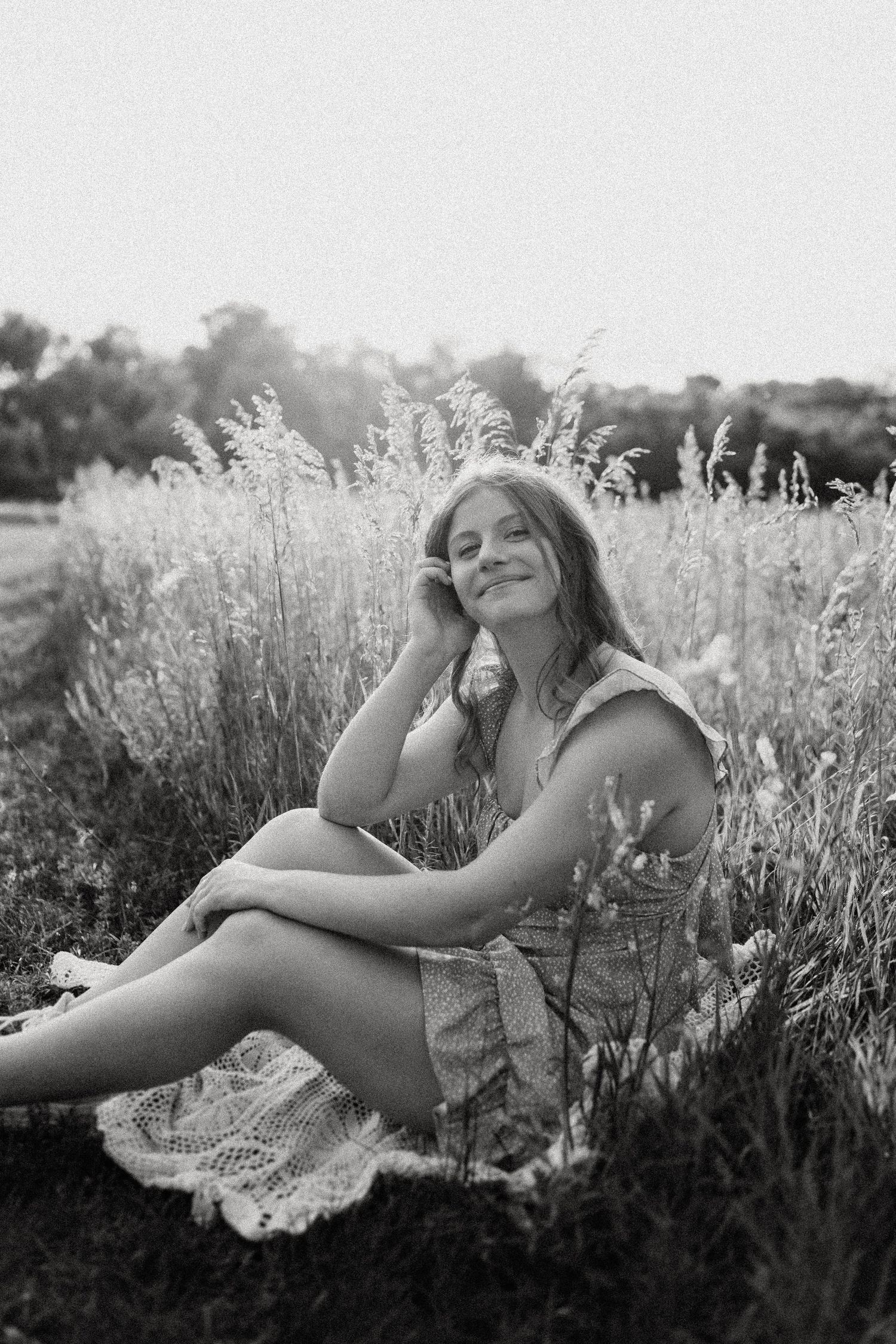 Black and white portrait of someone relaxing on blanket among tall meadow grasses.