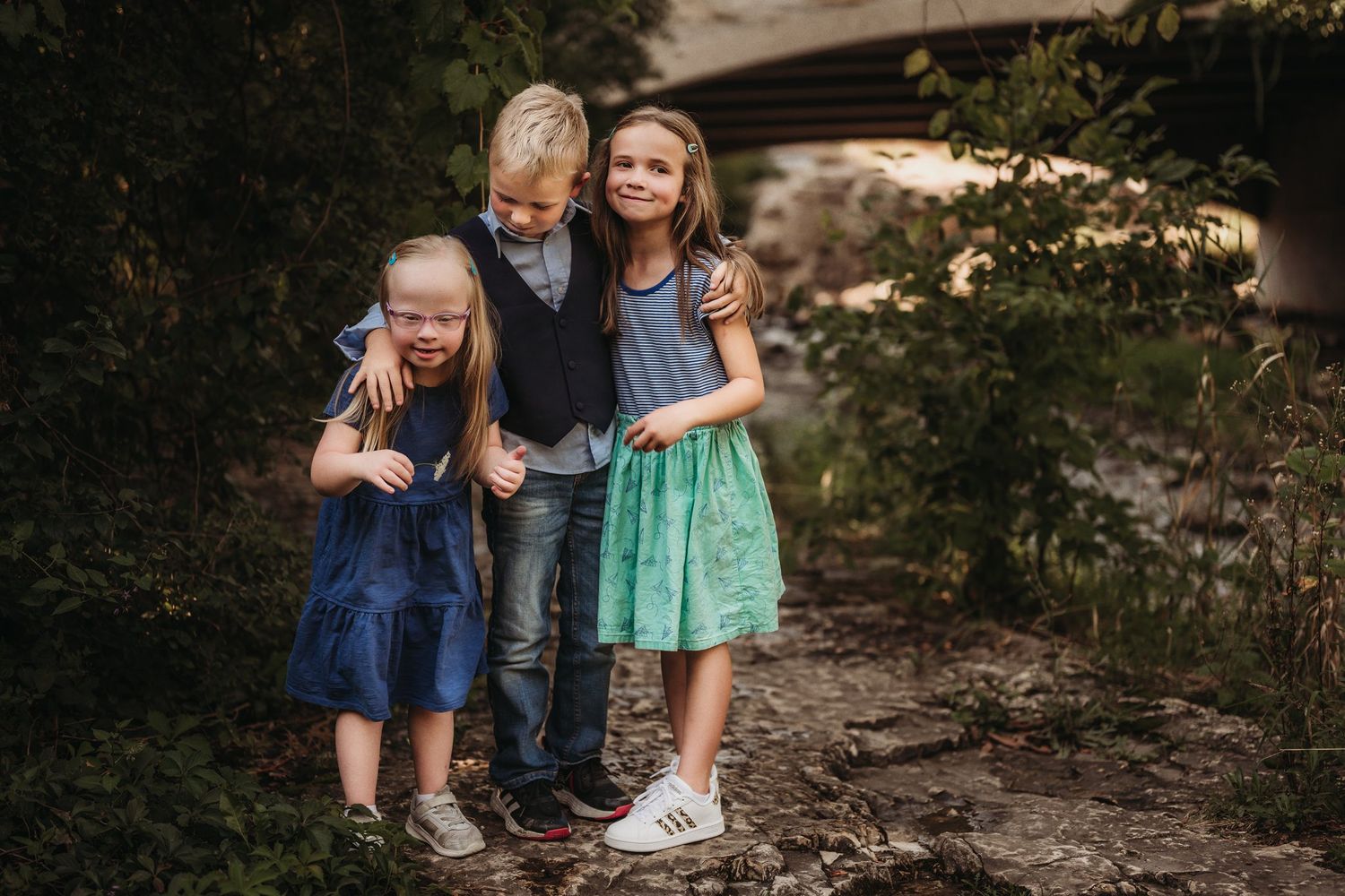Children pose together on a wooded trail beneath a bridge.