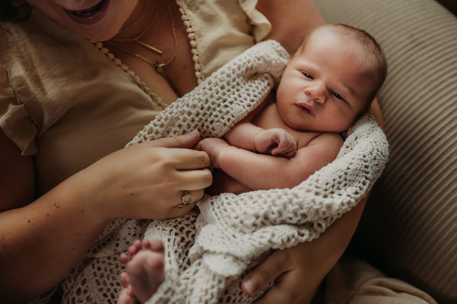 Newborn baby wrapped in a knitted blanket being cradled on a comfortable couch.