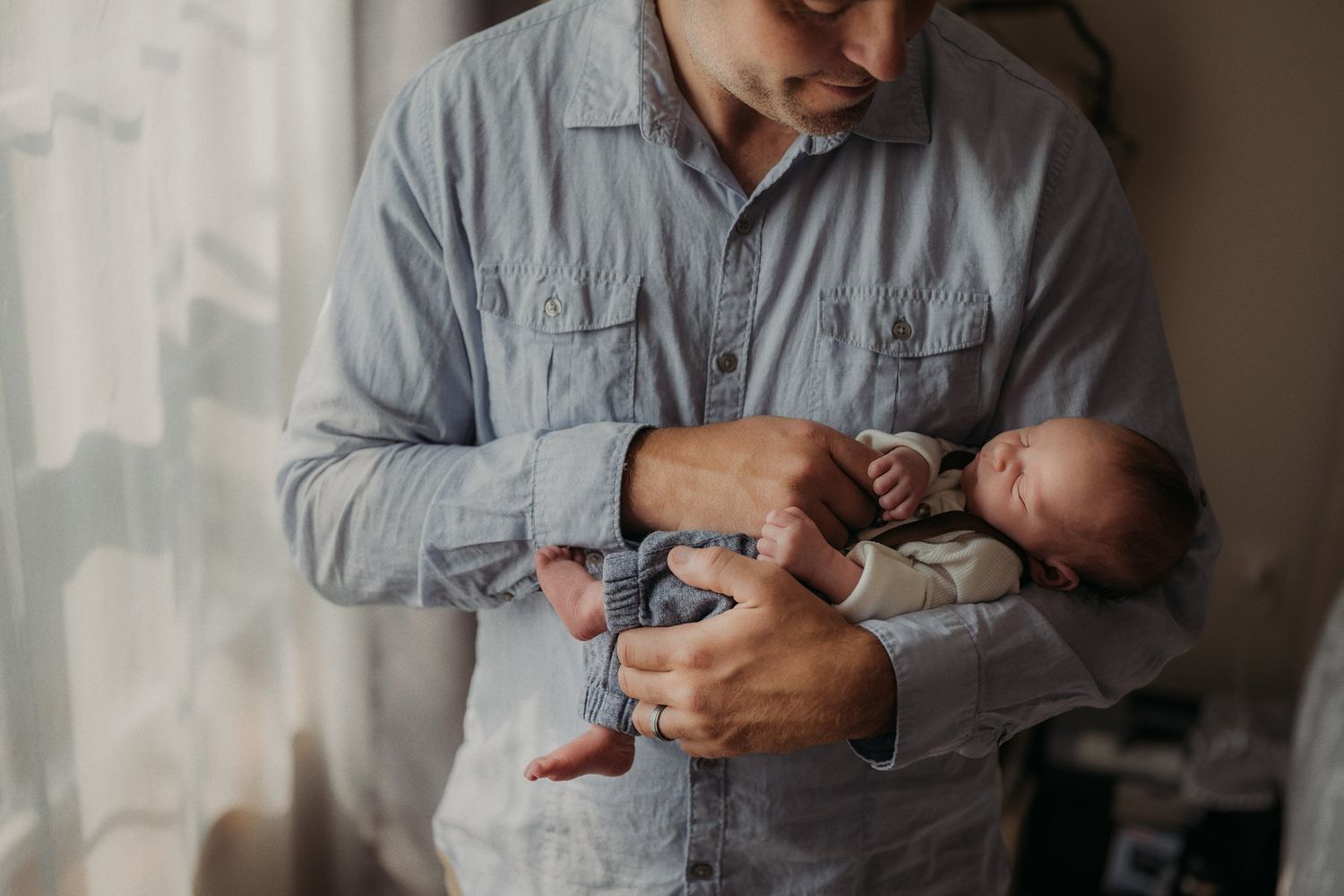 Parent in gray shirt carefully holds sleeping newborn baby.