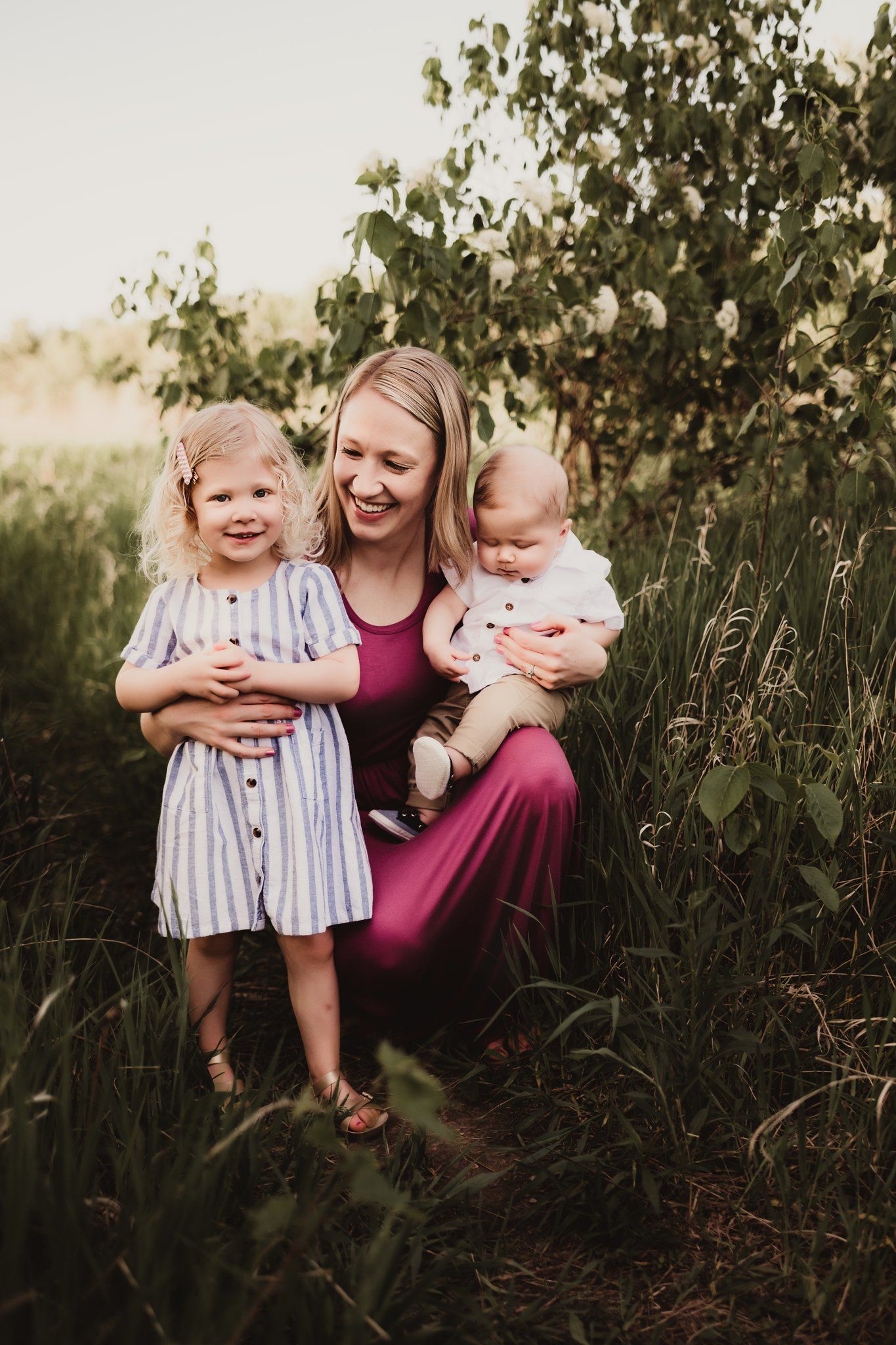 Joyful outdoor family moment captured in tall grass with burgundy dress and striped outfit details.