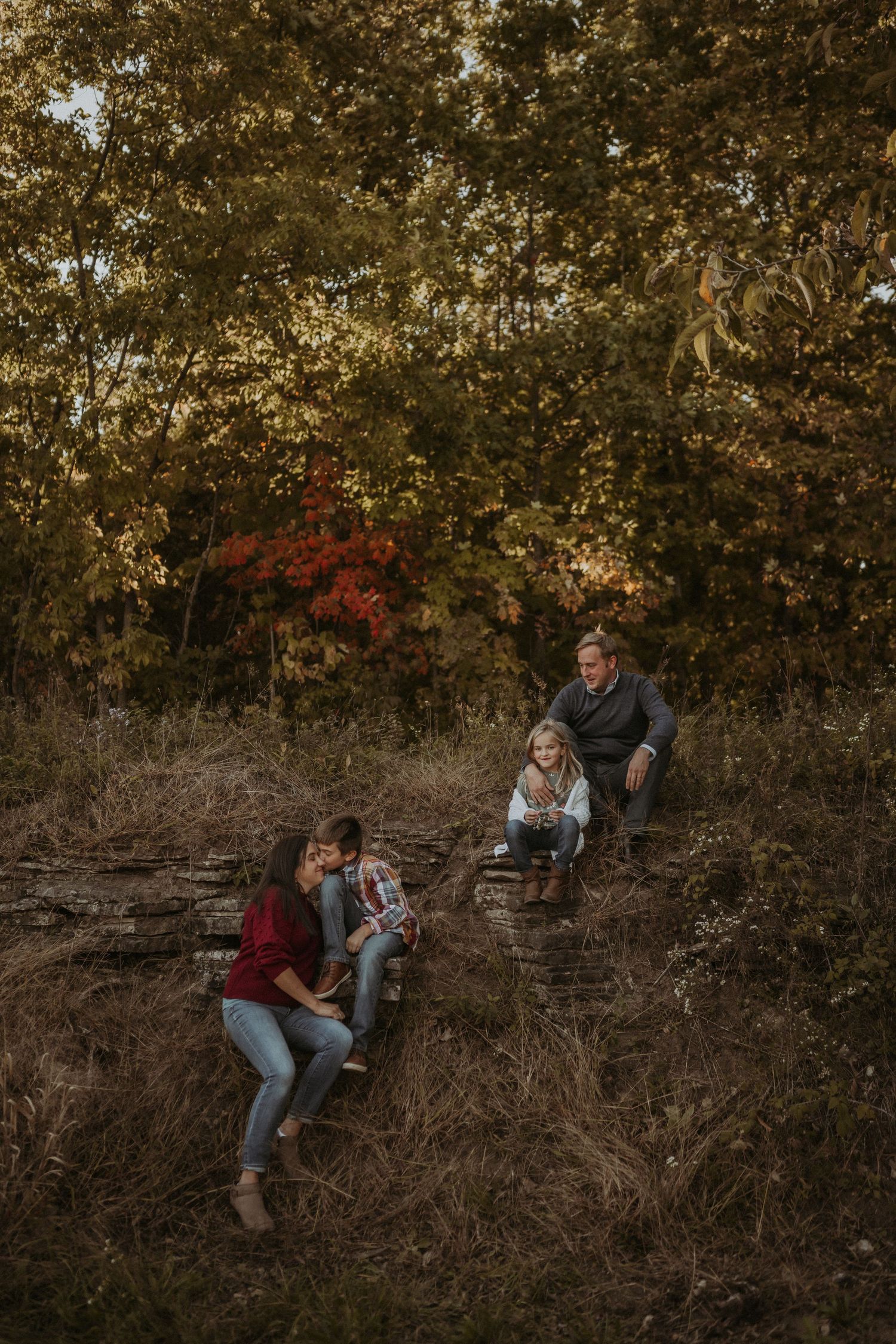 Family relaxing together on hillside during golden hour autumn photoshoot.