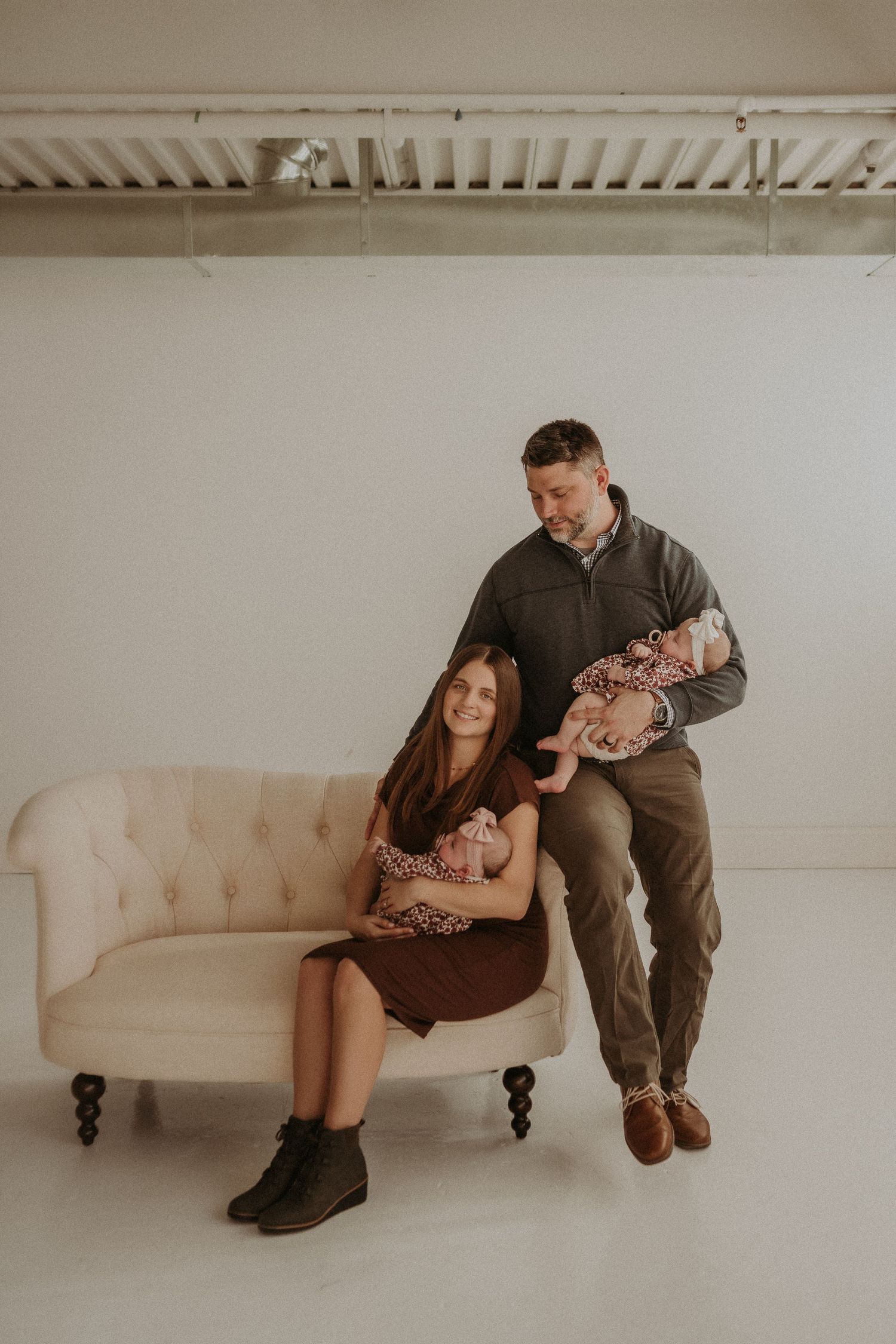 A family poses with twin babies on a vintage cream-colored sofa in a bright studio.