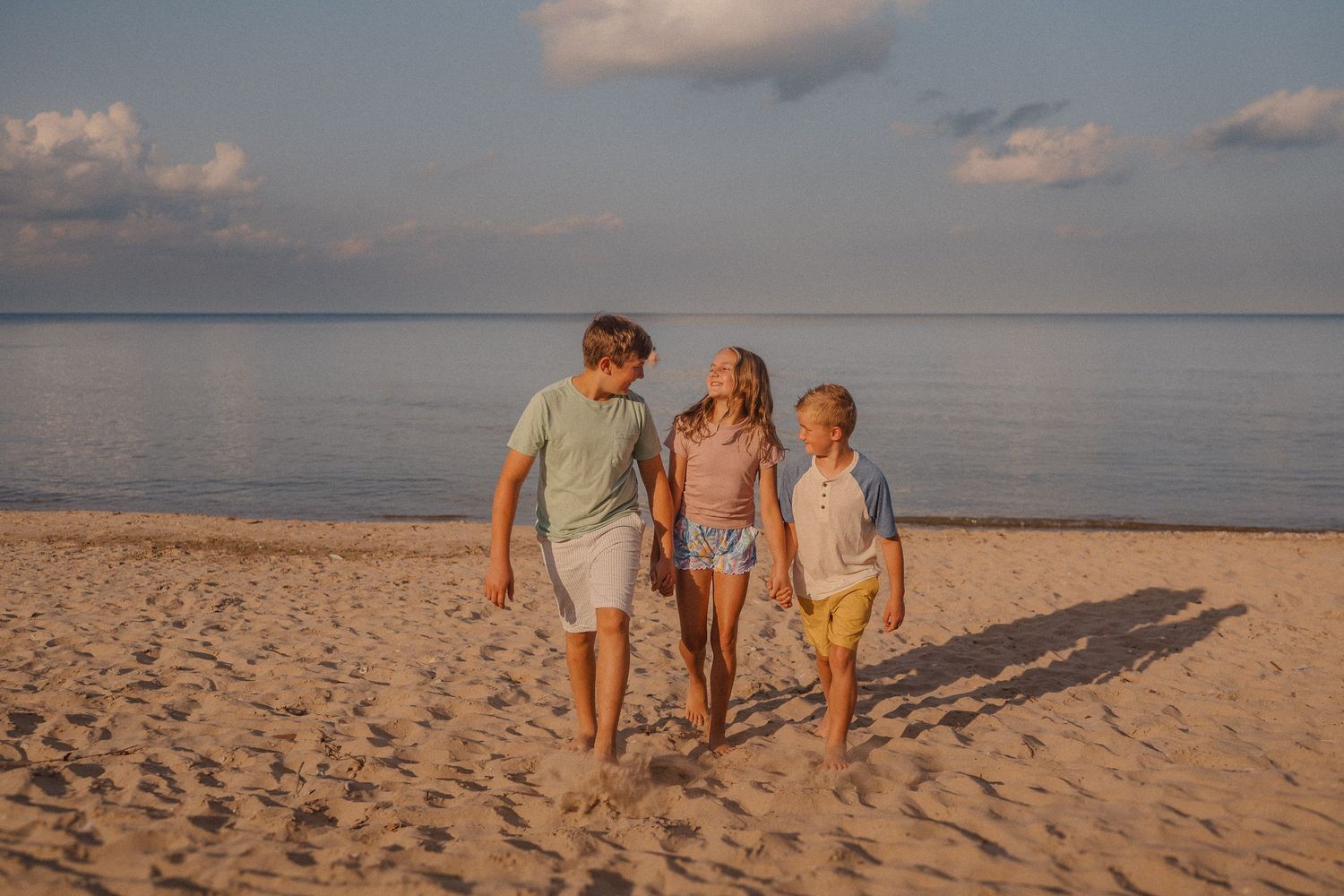Three people walking along a serene beach shoreline at sunset with footprints in the sand.
