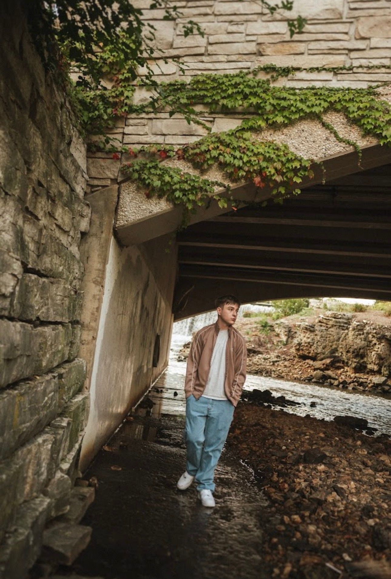 Moody portrait under a stone bridge surrounded by fallen autumn leaves.