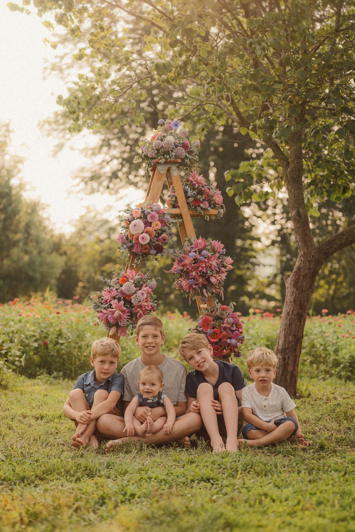 Children lounging on grass near floral decorated wooden stands during golden hour photoshoot.