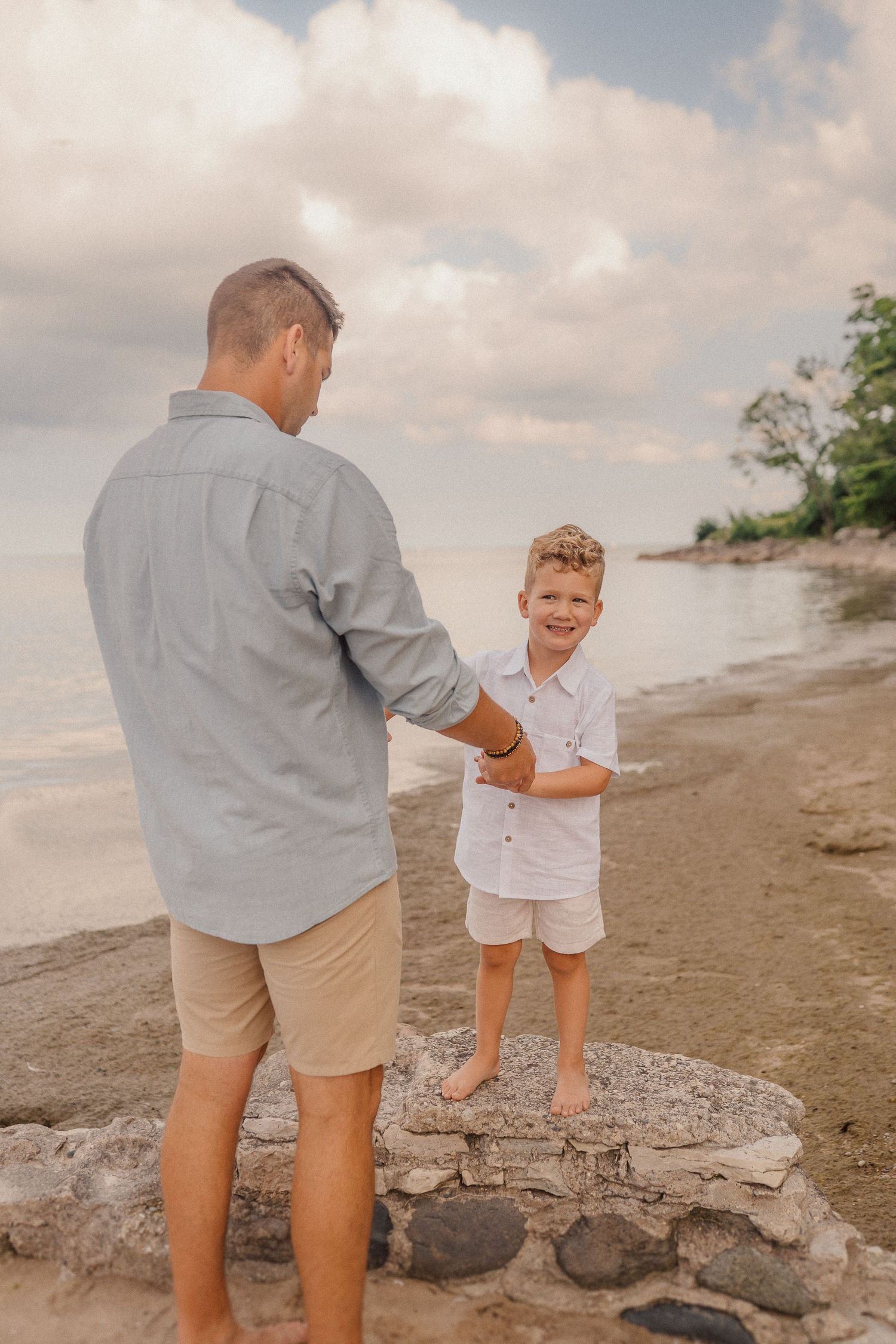 A beachside moment captured between a parent and child standing on rocky shoreline.