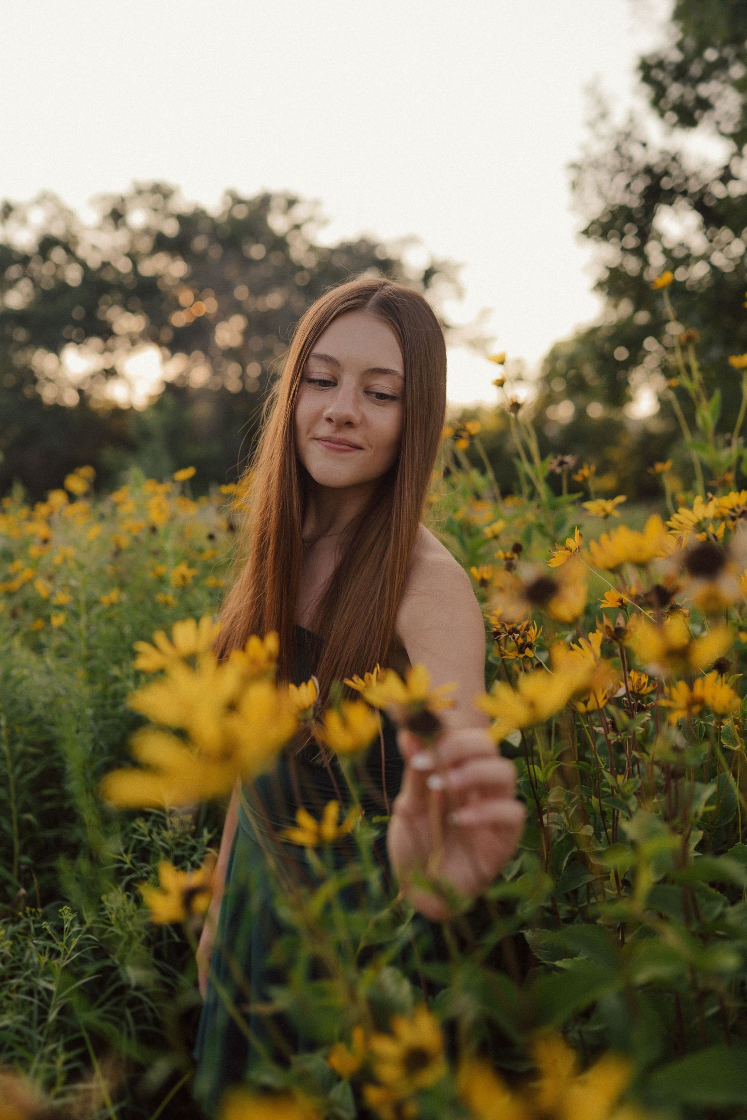 A person poses dreamily among bright yellow wildflowers in a golden-hour garden setting.