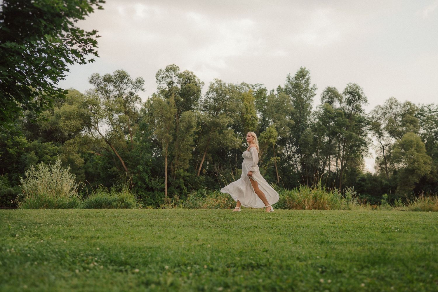 Figure in white dress standing in a serene green meadow at dusk.