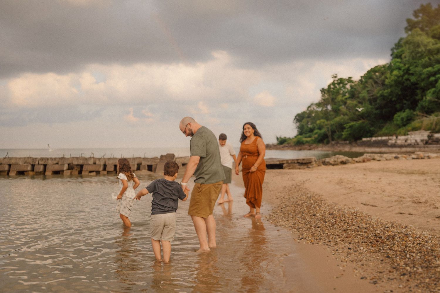 A family splashes and plays together in shallow ocean water at sunset along a sandy beach.
