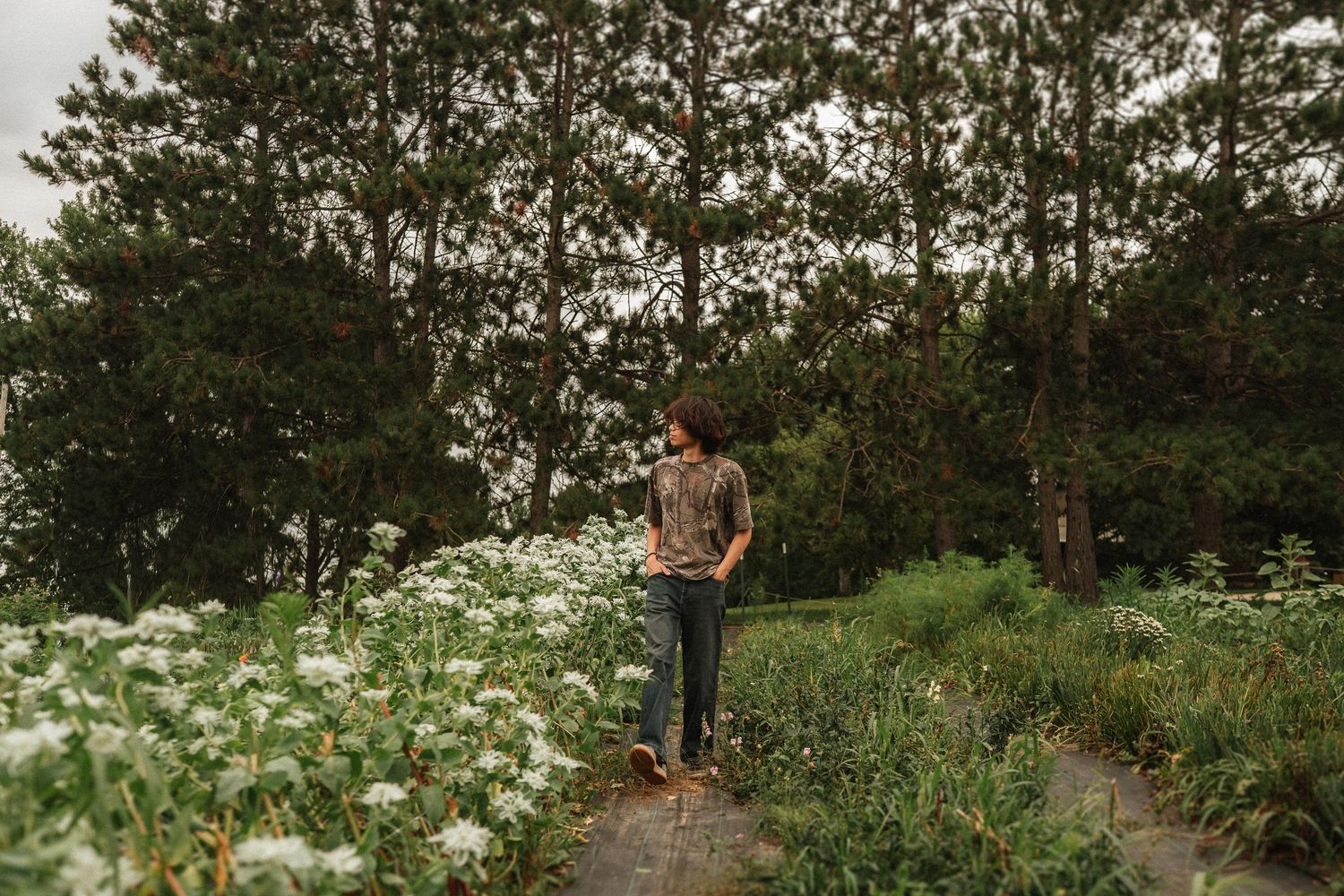 A couple poses together in a lush green garden filled with white wildflowers during a bright summer afternoon.