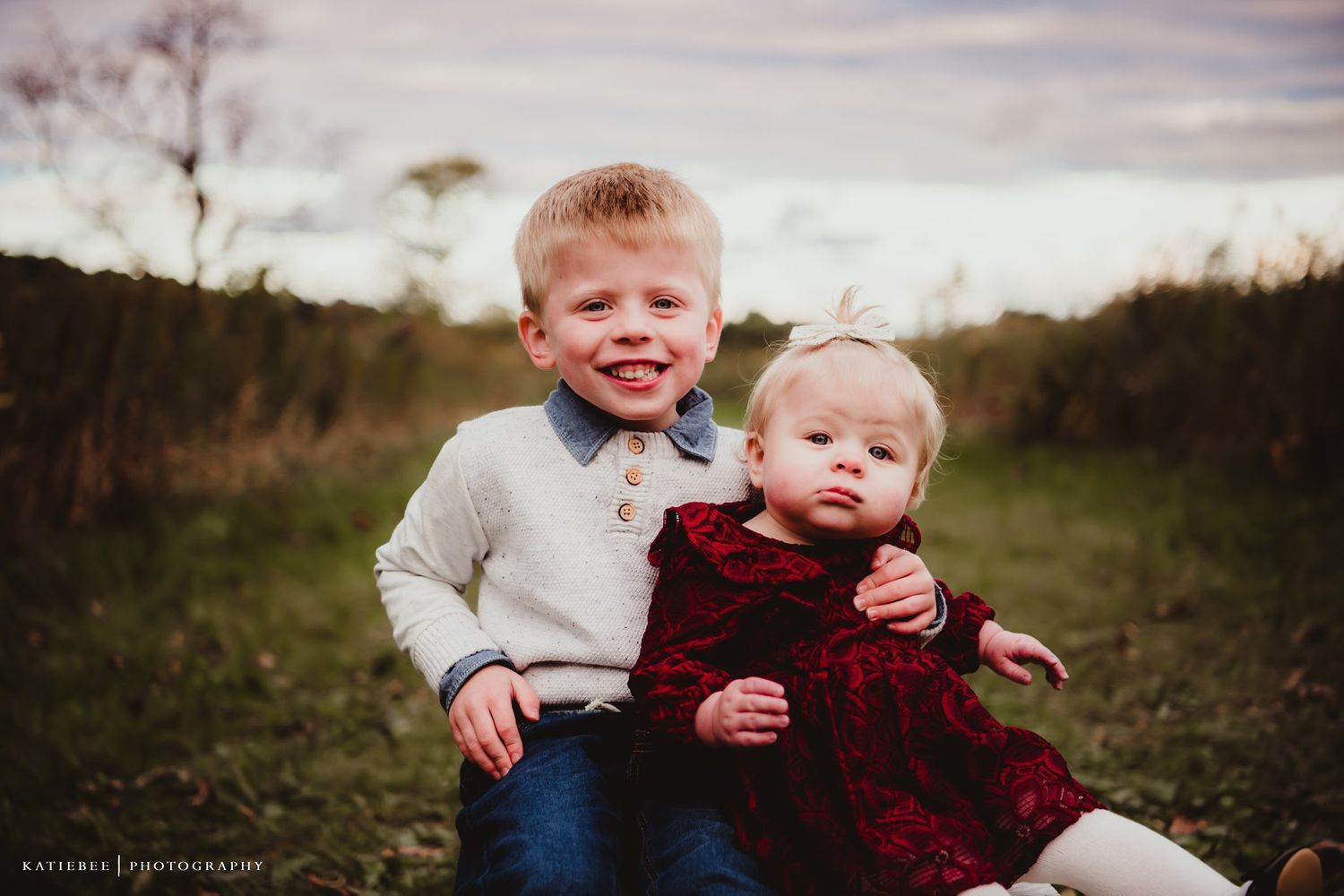 Two siblings pose together outdoors wearing coordinating outfits on an overcast autumn day.