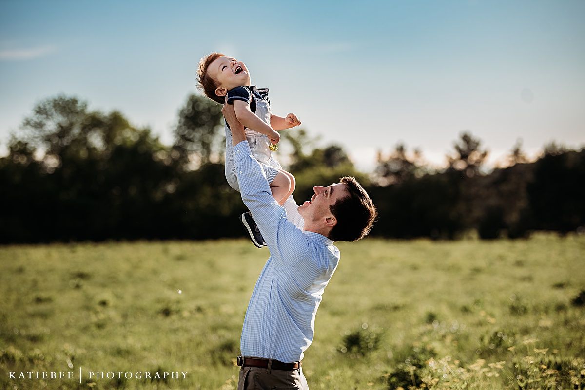 Playful lift against blue sky in grassy field during golden hour photography session.