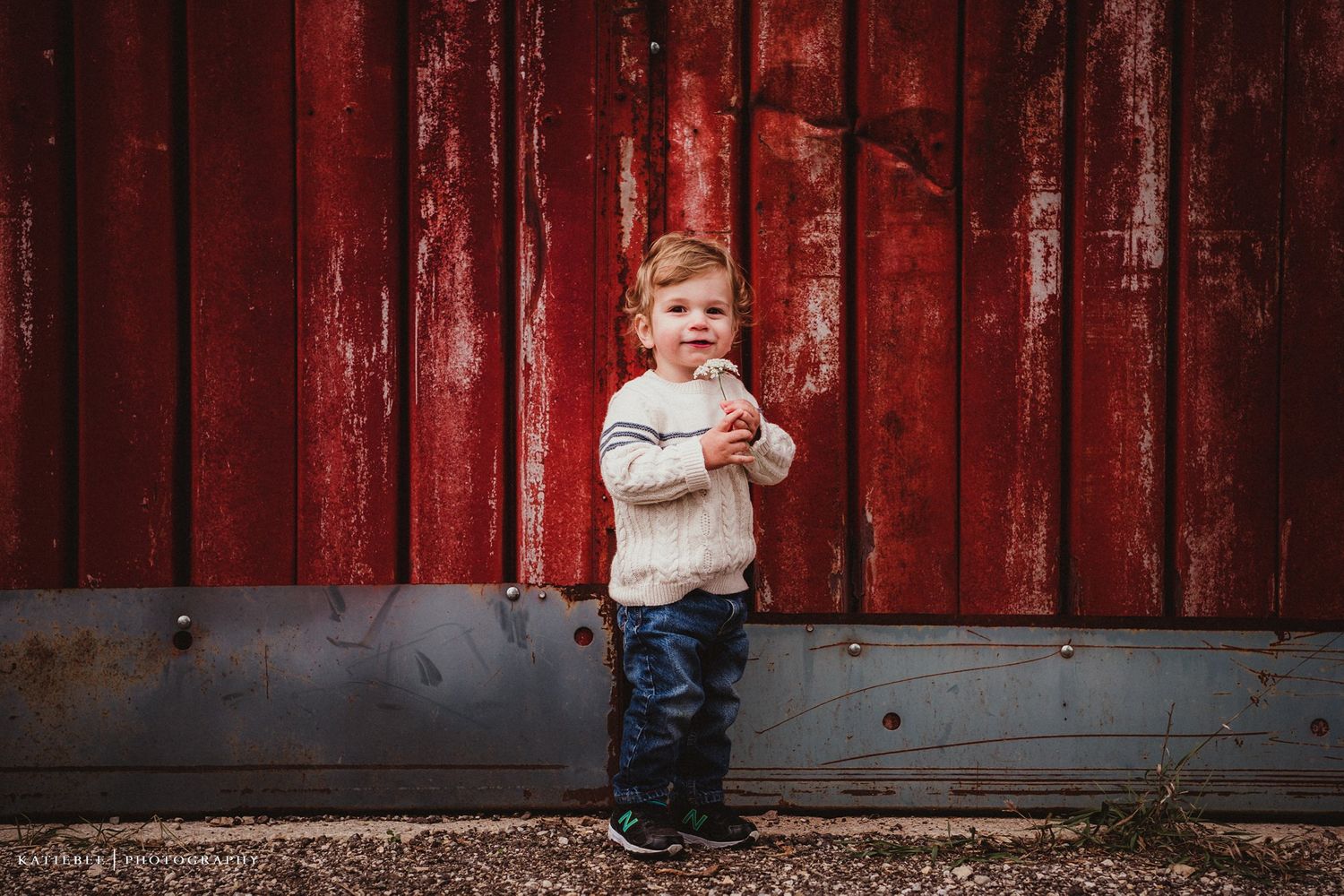 Small figure in winter boots standing against distressed red barn wall.